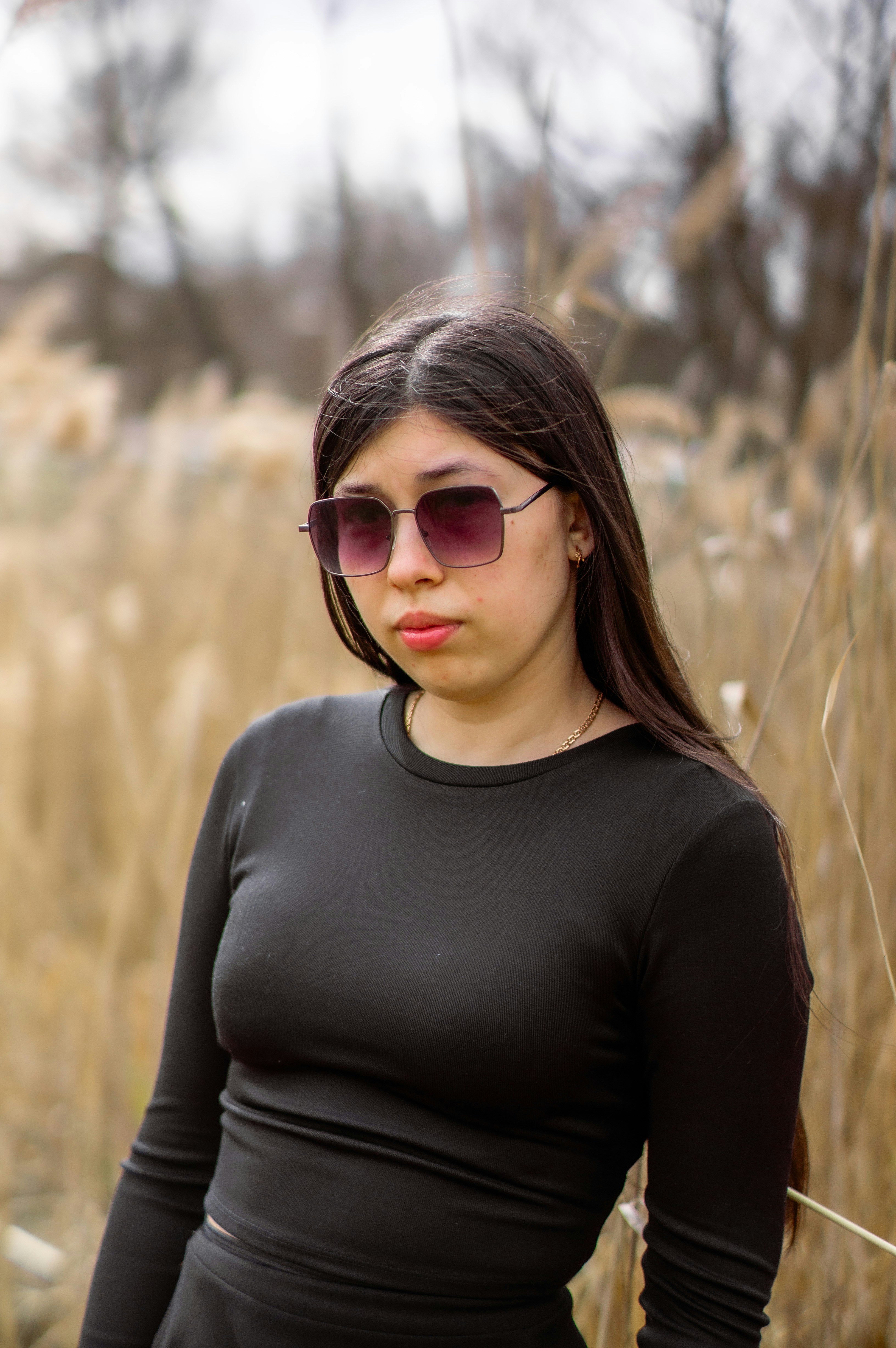 Eine Frau mit Sonnenbrille posiert im hohen Gras.