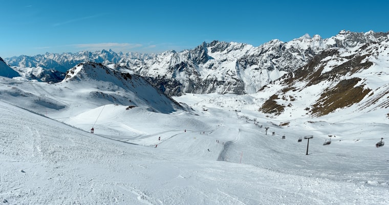 A wide snowy ski area with chairlifts and scattered skiers beneath a ring of rocky peaks