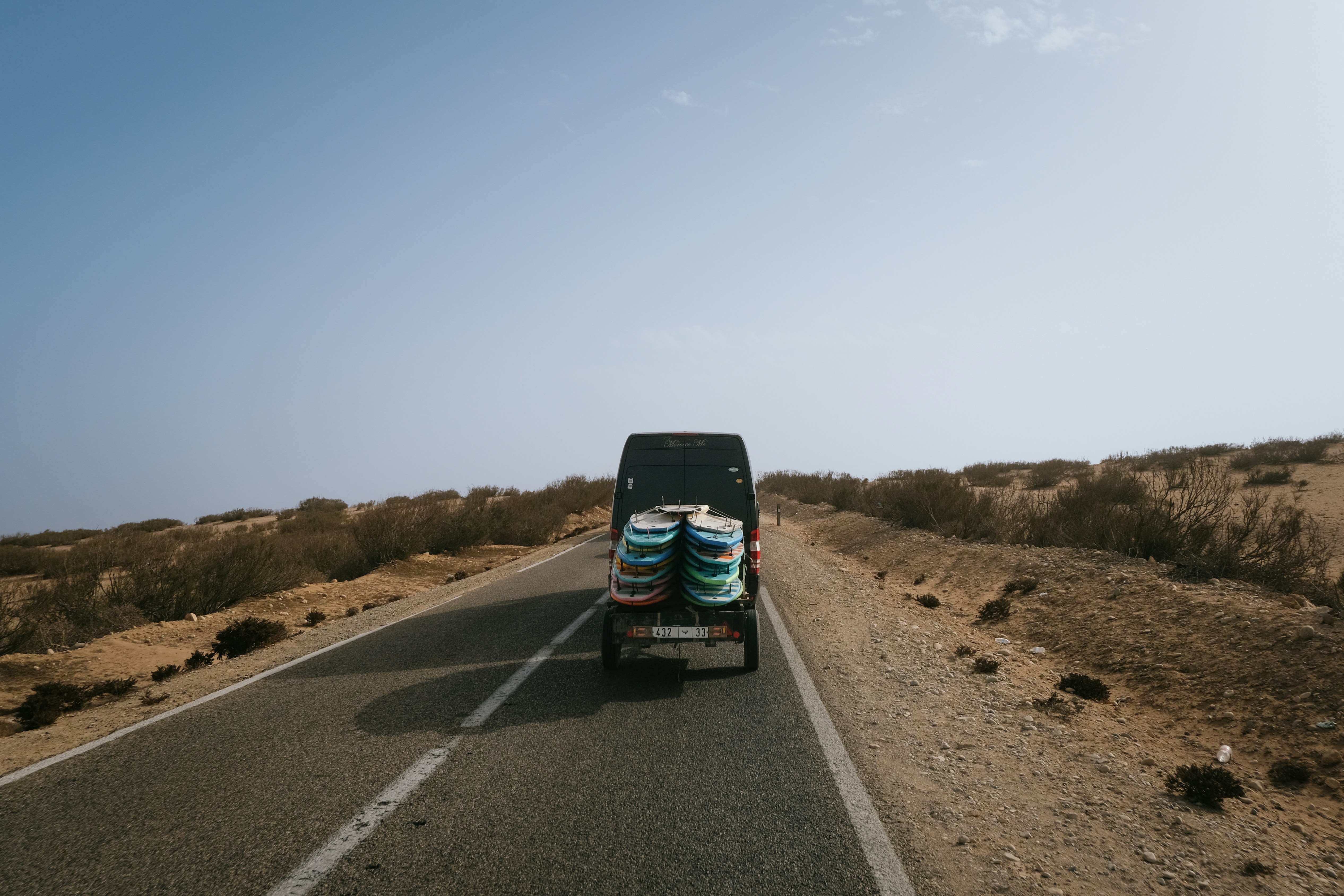 A van with surfboards drives down a desert road.