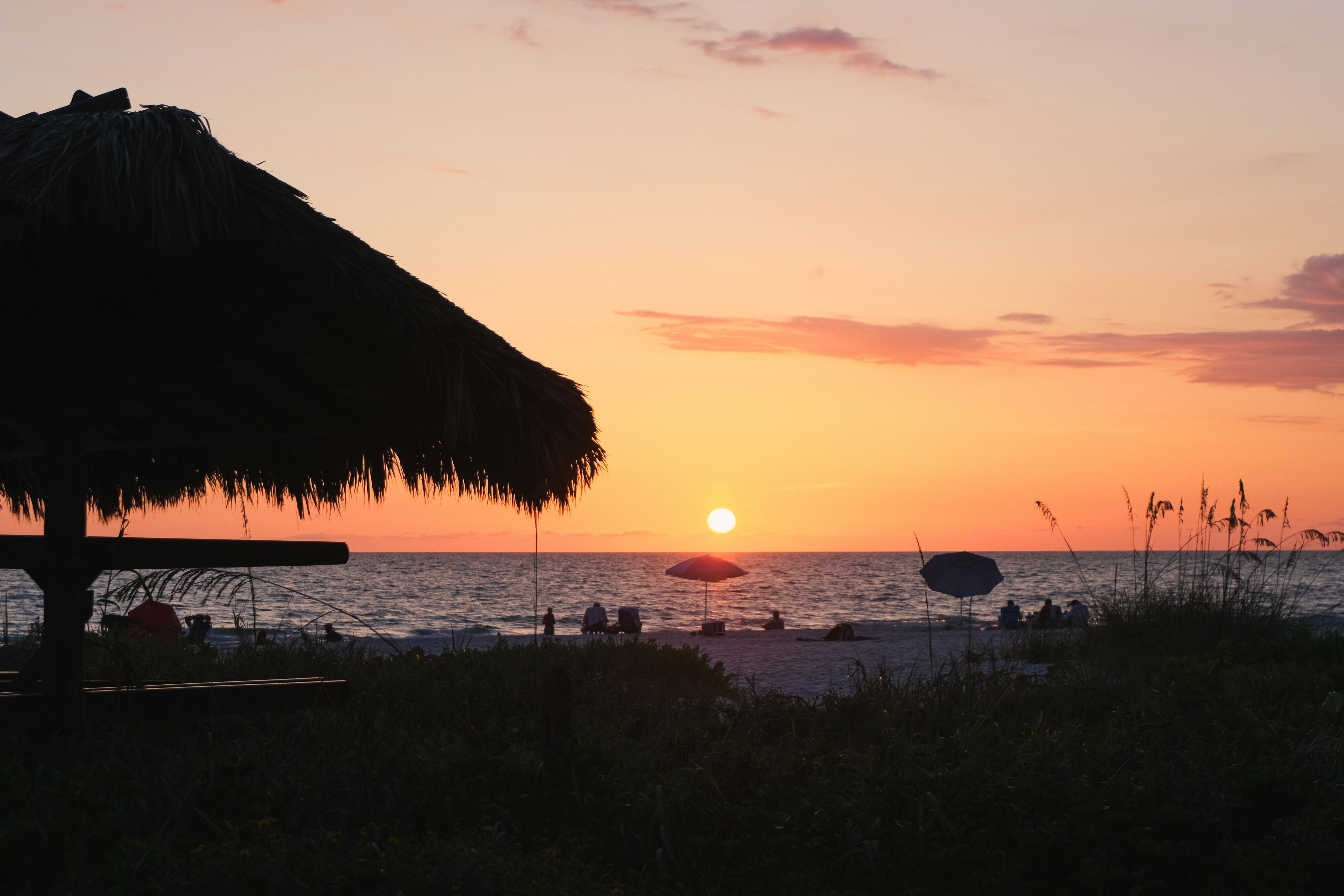 Sunset illuminates a beach with a tiki hut.