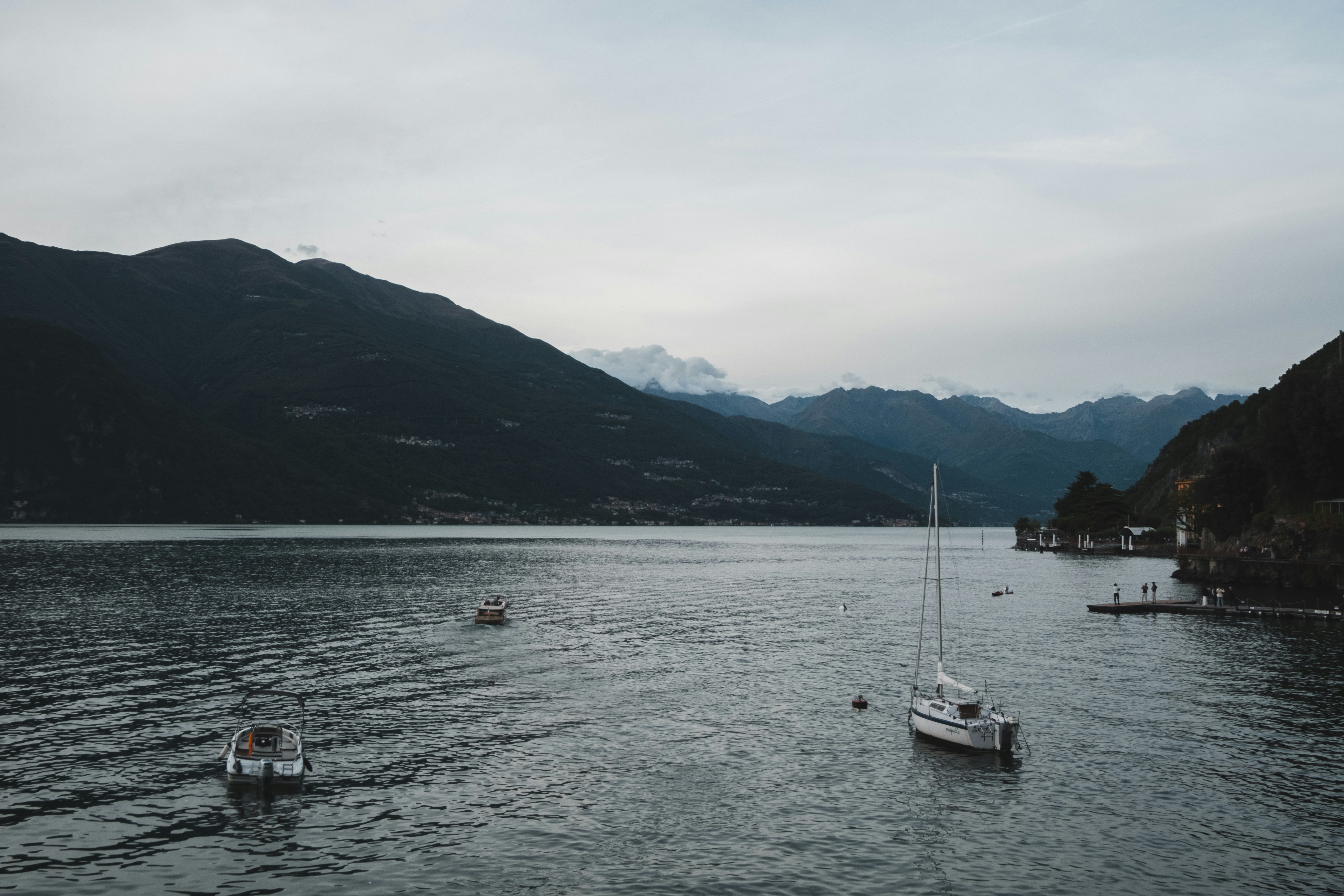 Boats sail on a lake against a mountain backdrop.