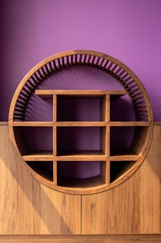 A wooden, circular shelf against a purple wall.