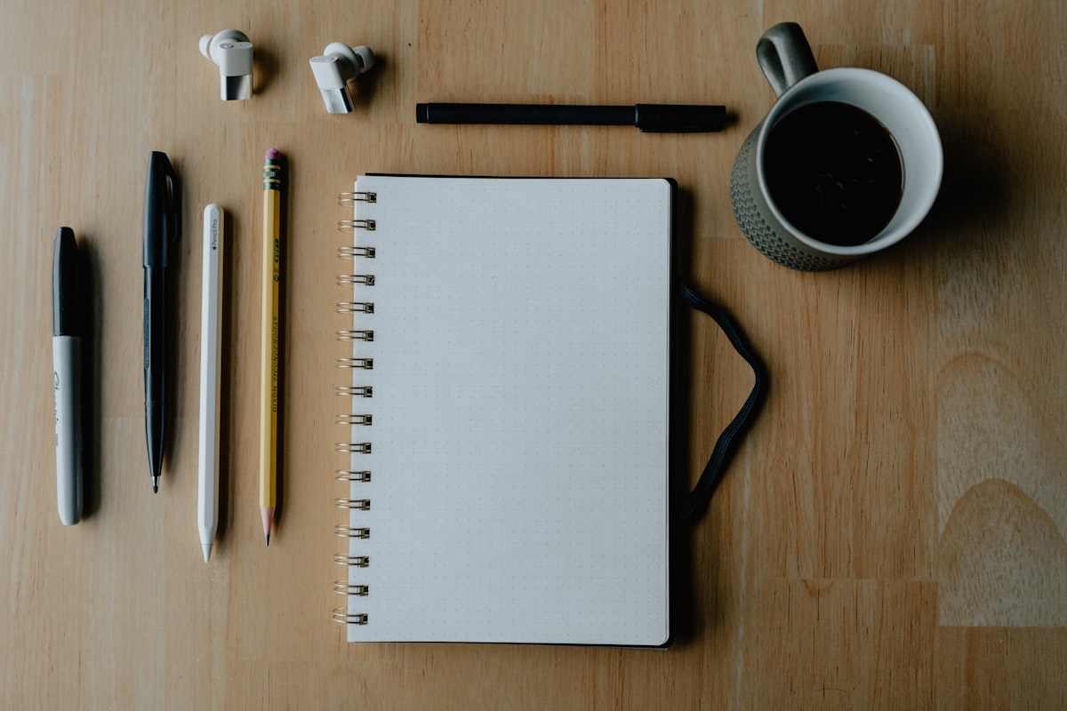 Notizbuch, Stifte und Kaffee auf einem Schreibtisch als Symbol für einen klaren Plan