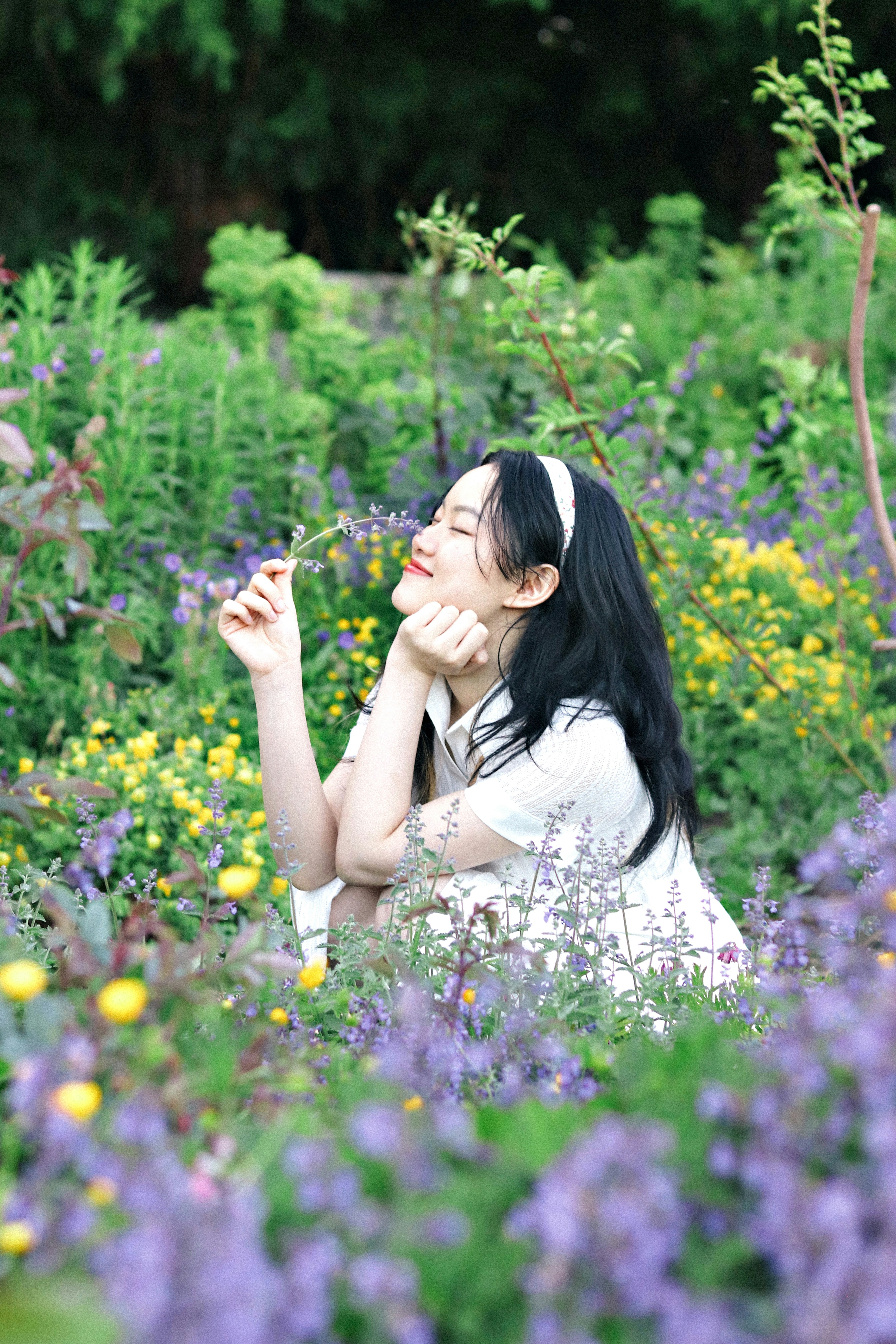 Eine Frau lächelt zwischen Blumen in einem Garten.