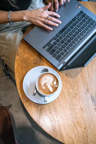 Woman works on laptop with a latte nearby.
