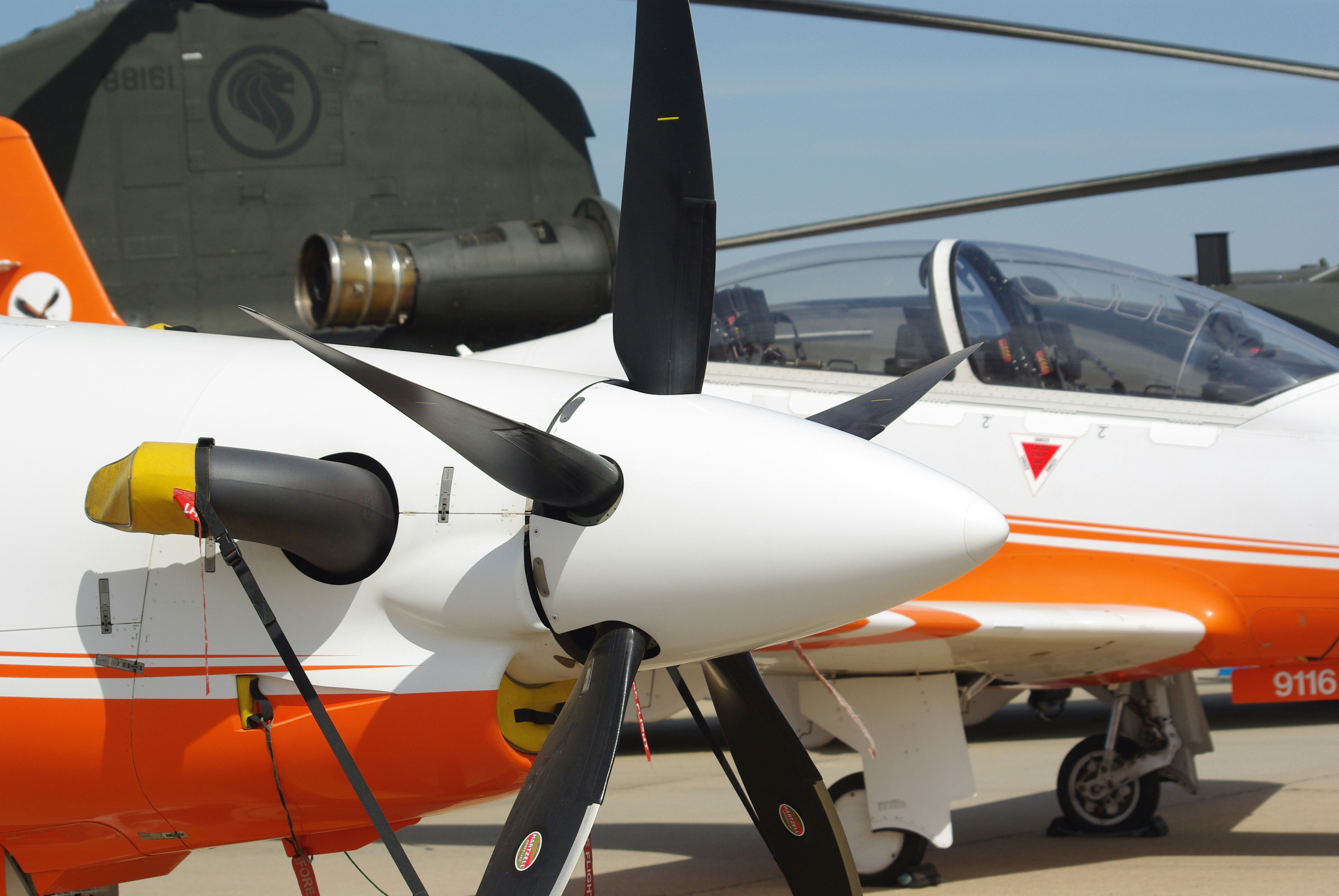 A propeller plane is in front of a military helicopter.