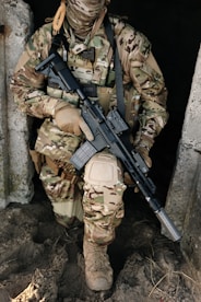 A soldier in combat gear holds a rifle.