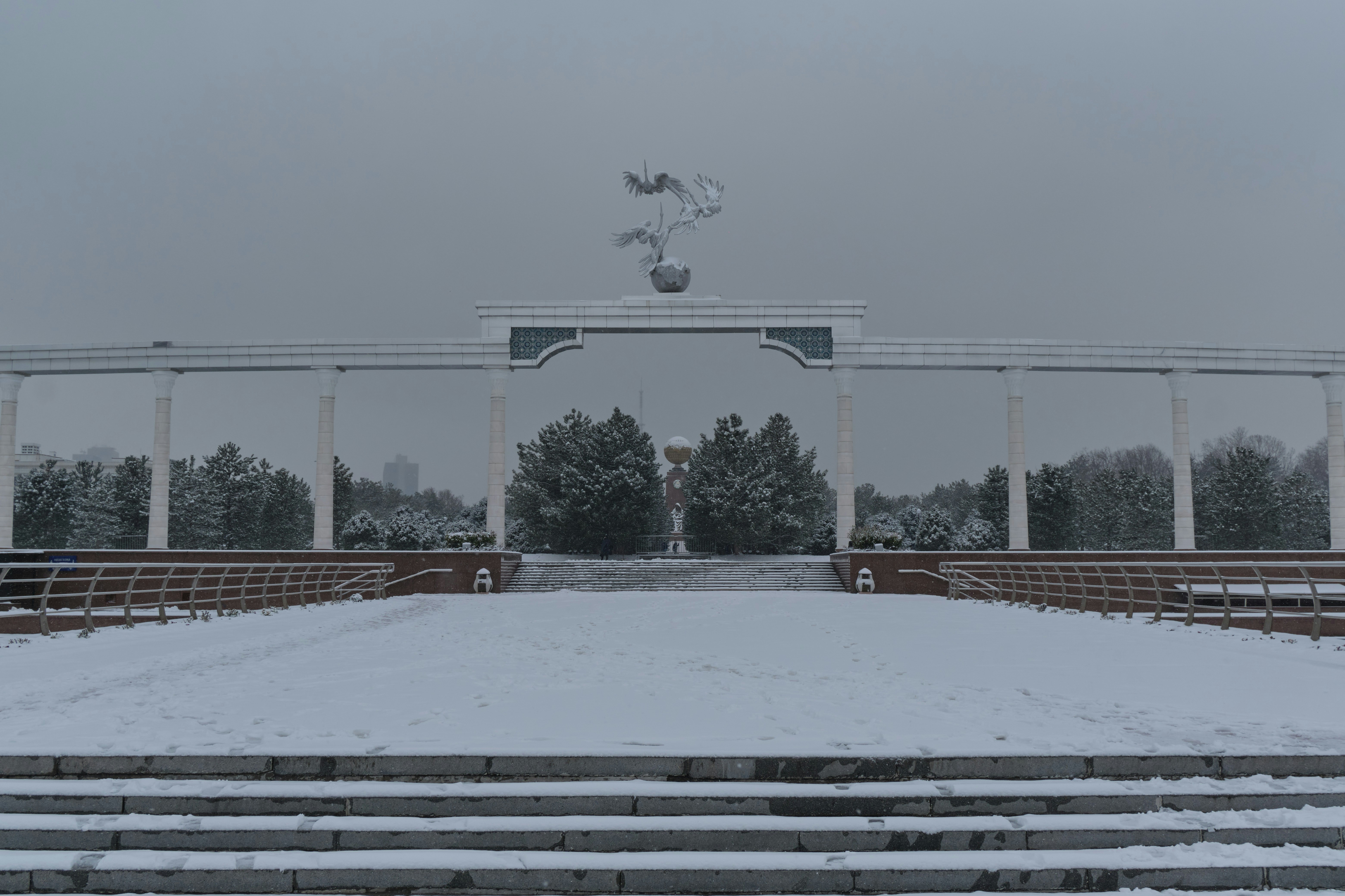 Snow covers a park's entrance with a monument.
