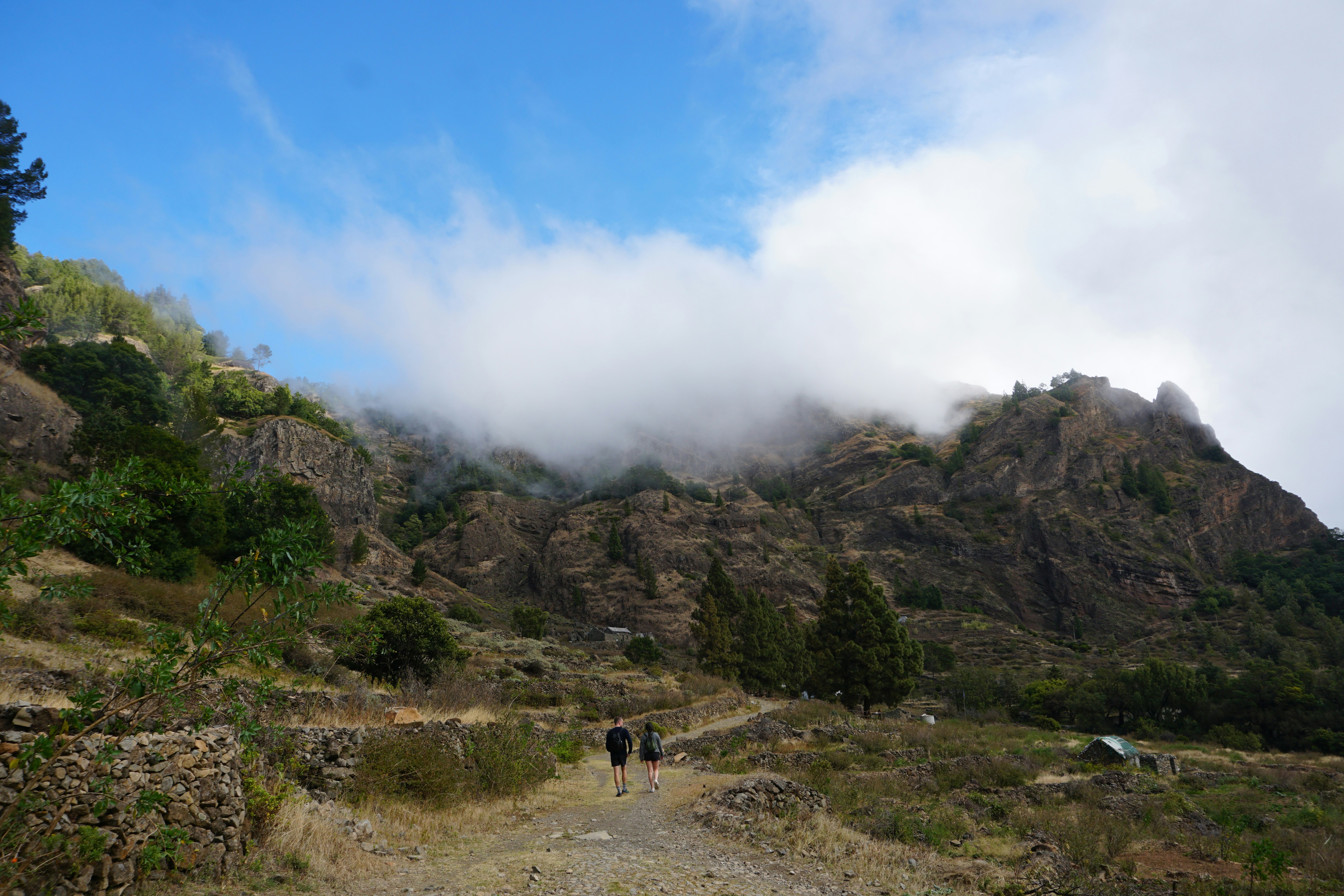 Clouds roll over a mountainous landscape with hikers.