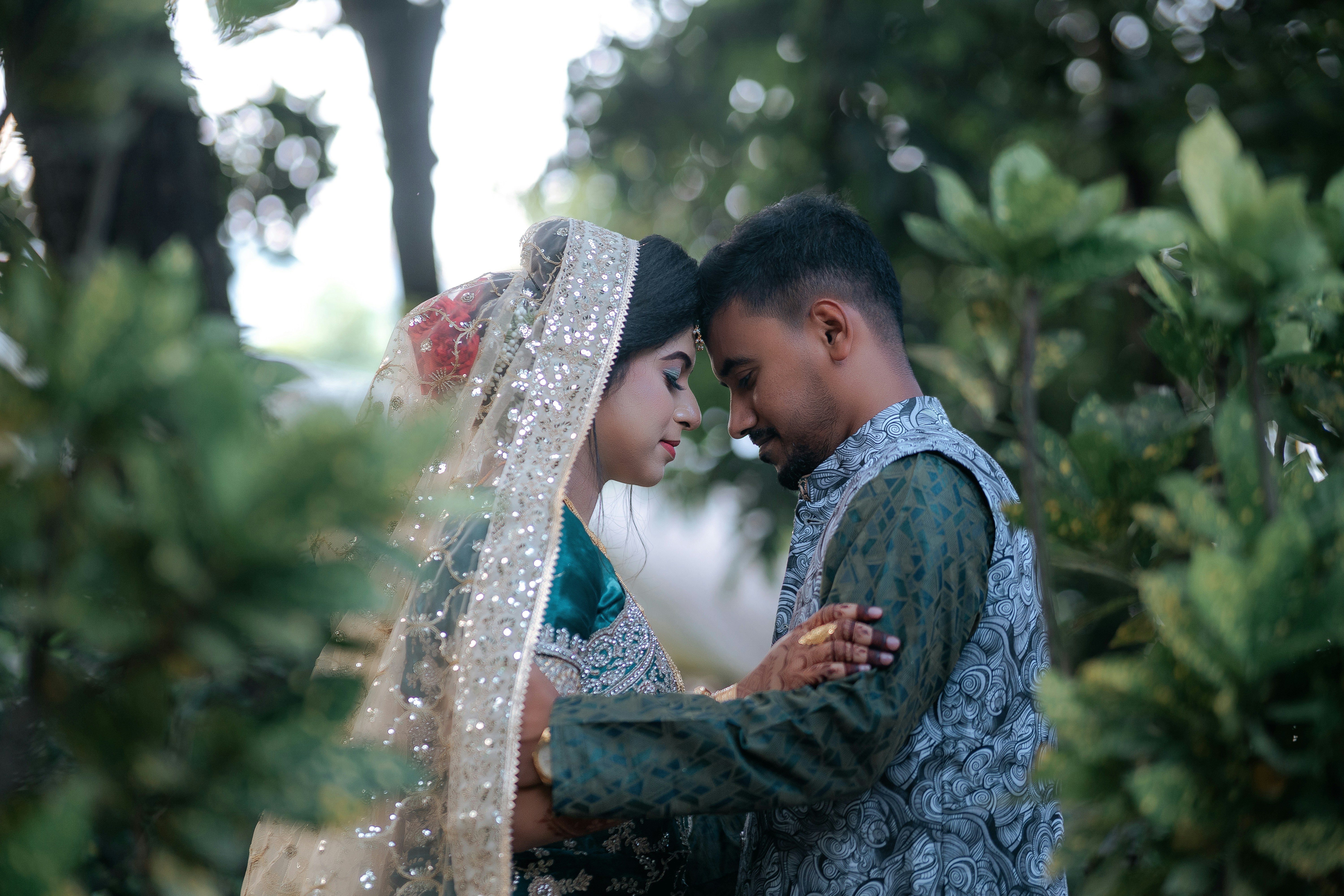 A newlywed couple embraces amidst the greenery.