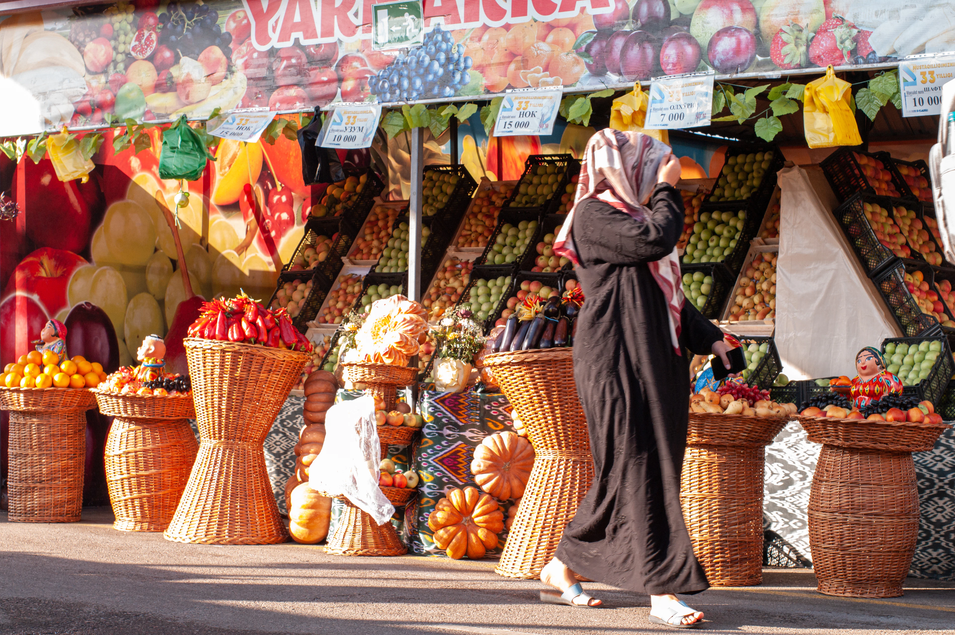 A fruit stall at a Tashkent bazaar, woven baskets of pomegranates and squash stacked along the front under Uzbek signage