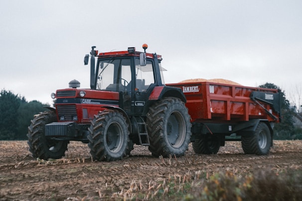 A red tractor pulls a loaded trailer.