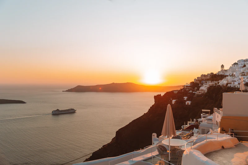 Cruise ship anchored off a whitewashed Greek island village at golden-hour sunset