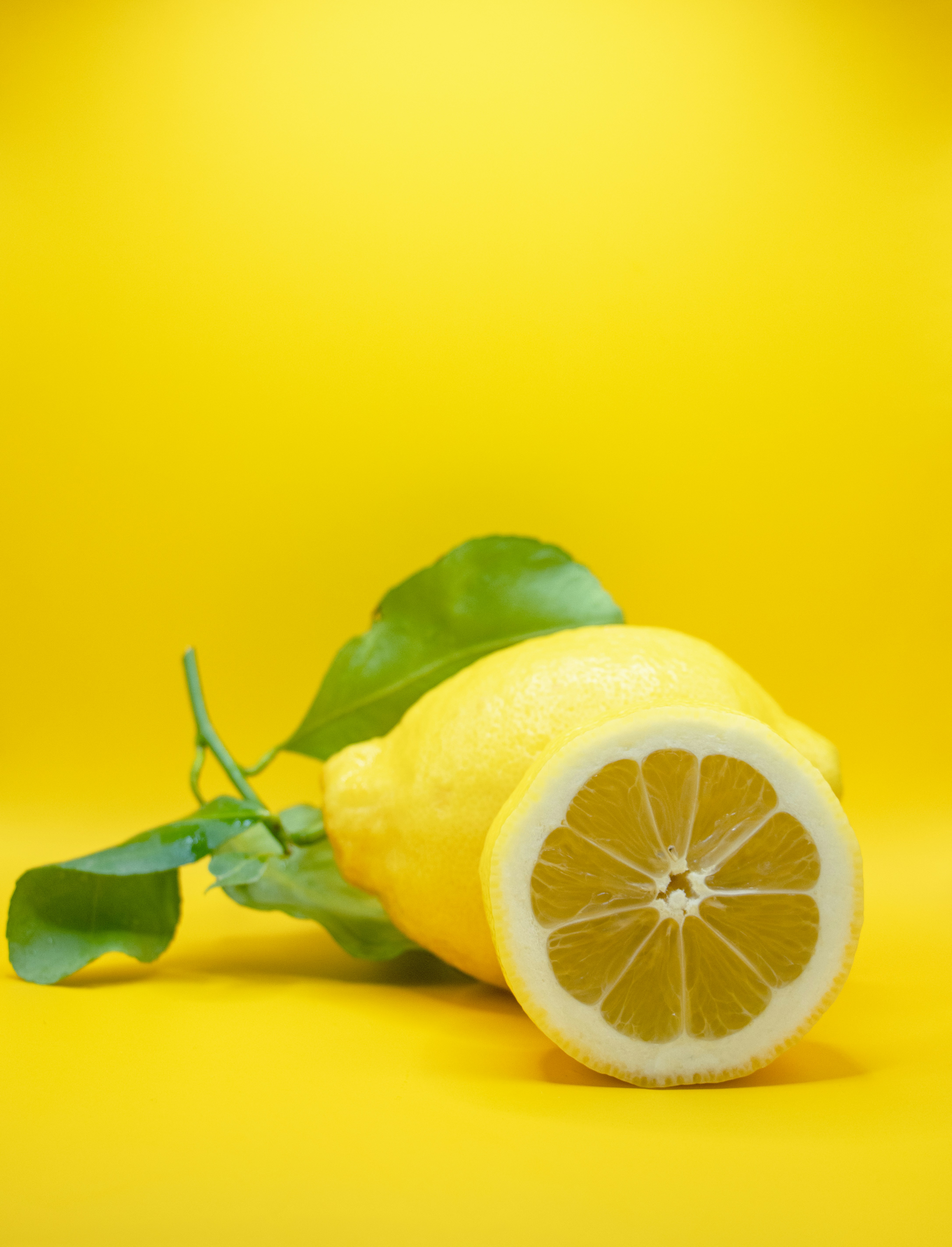Lemons with green leaves on a vibrant yellow background.