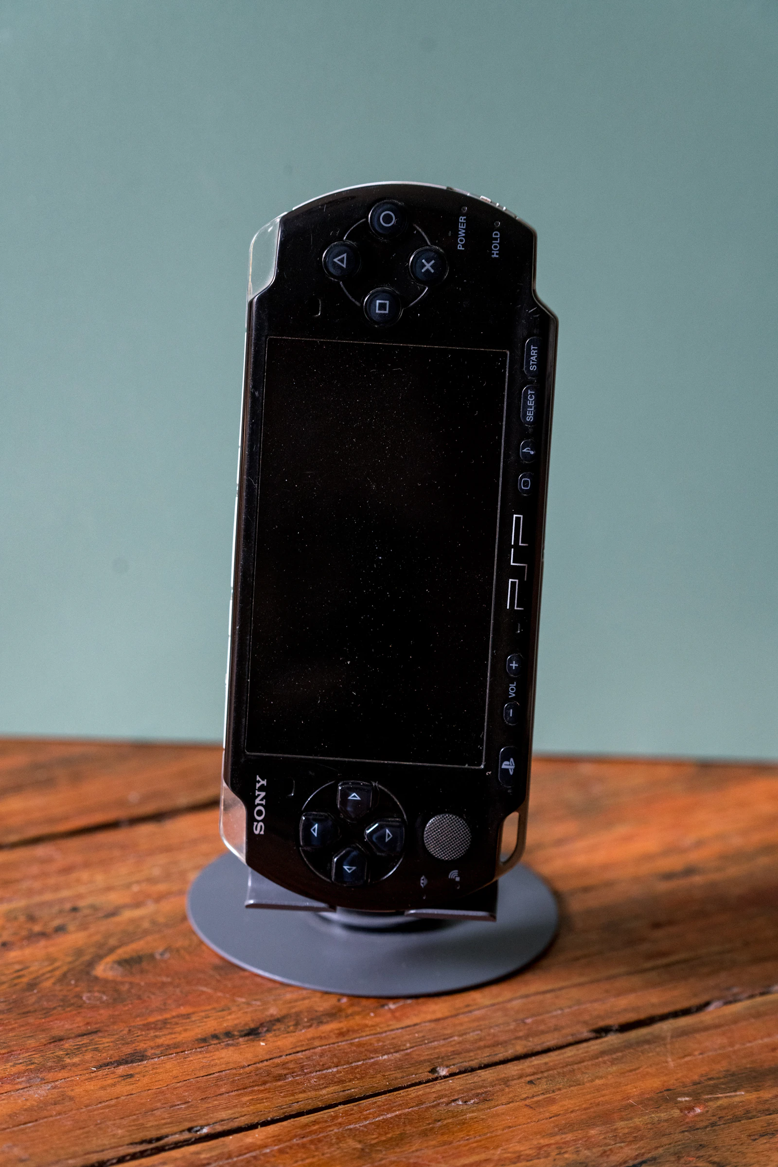 Black Sony PSP handheld console on display against a wood background