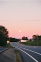 A road leads toward the moon in a pink sky.