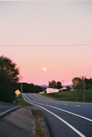 A road leads toward the moon in a pink sky.