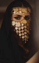 Woman wearing a veil and ornate gold jewelry.