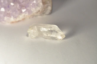 A clear crystal with purple quartz in the background.