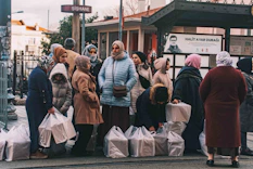 Women wait at a stop with groceries.