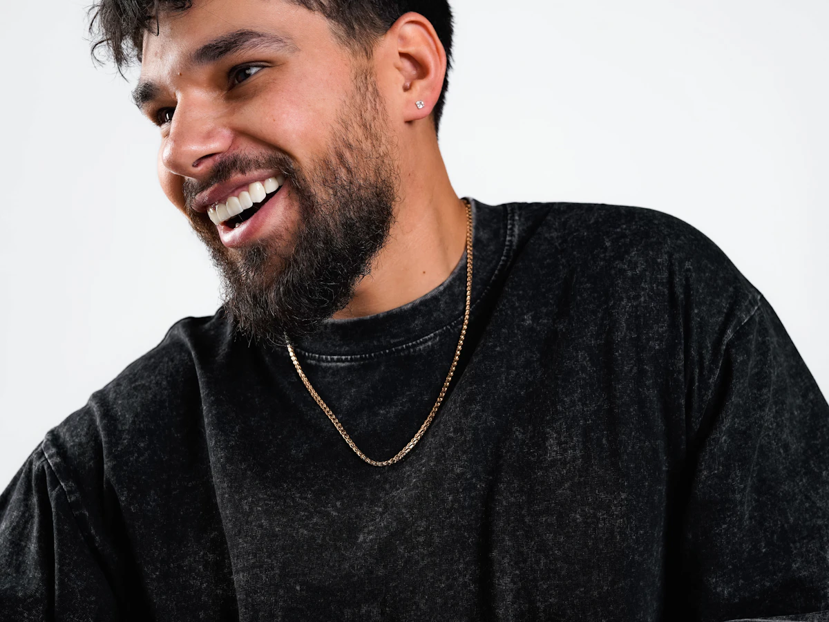 Smiling bearded man wearing a gold chain over a black knit shirt