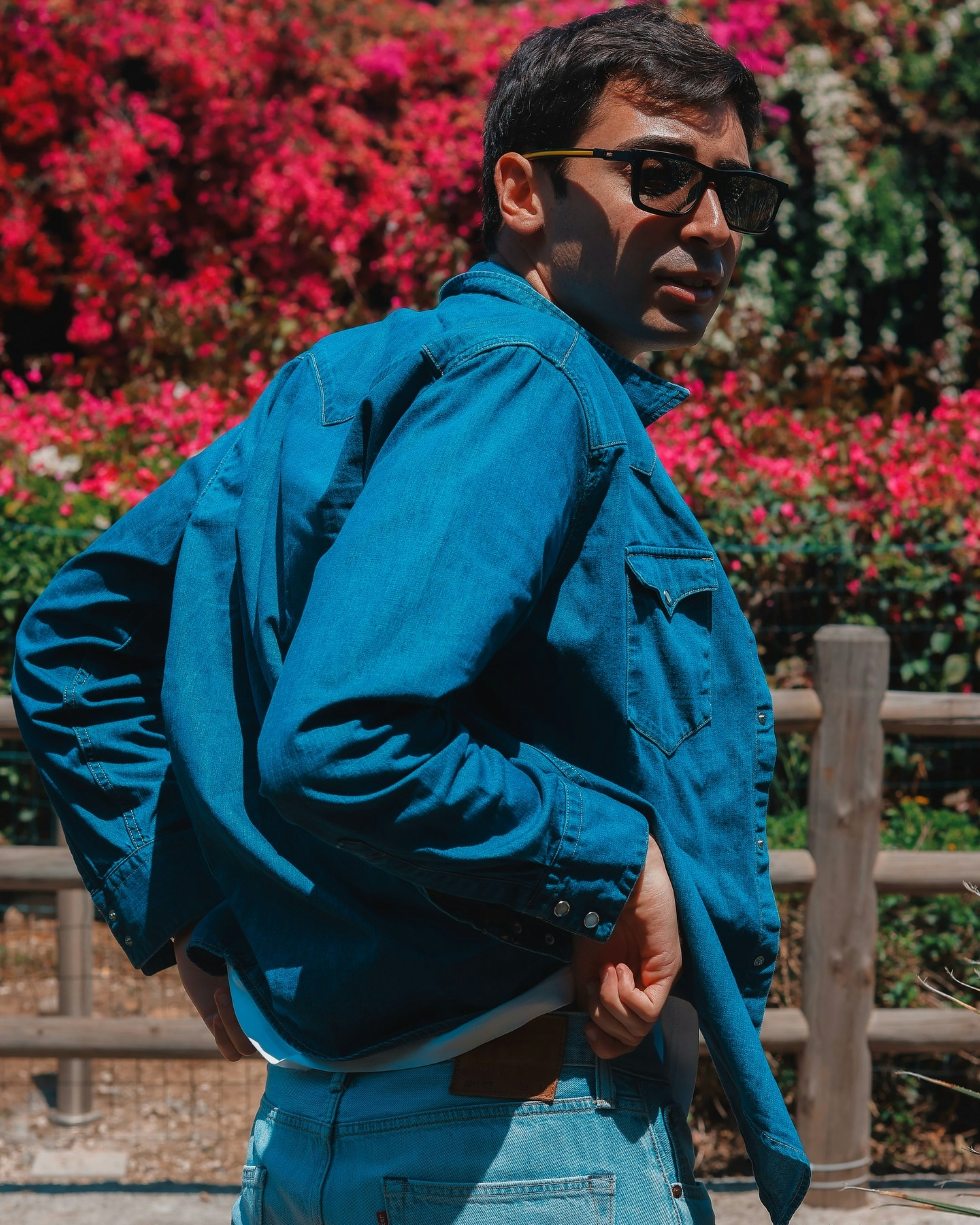 Mann in Jeansjacke posiert neben Blumen.