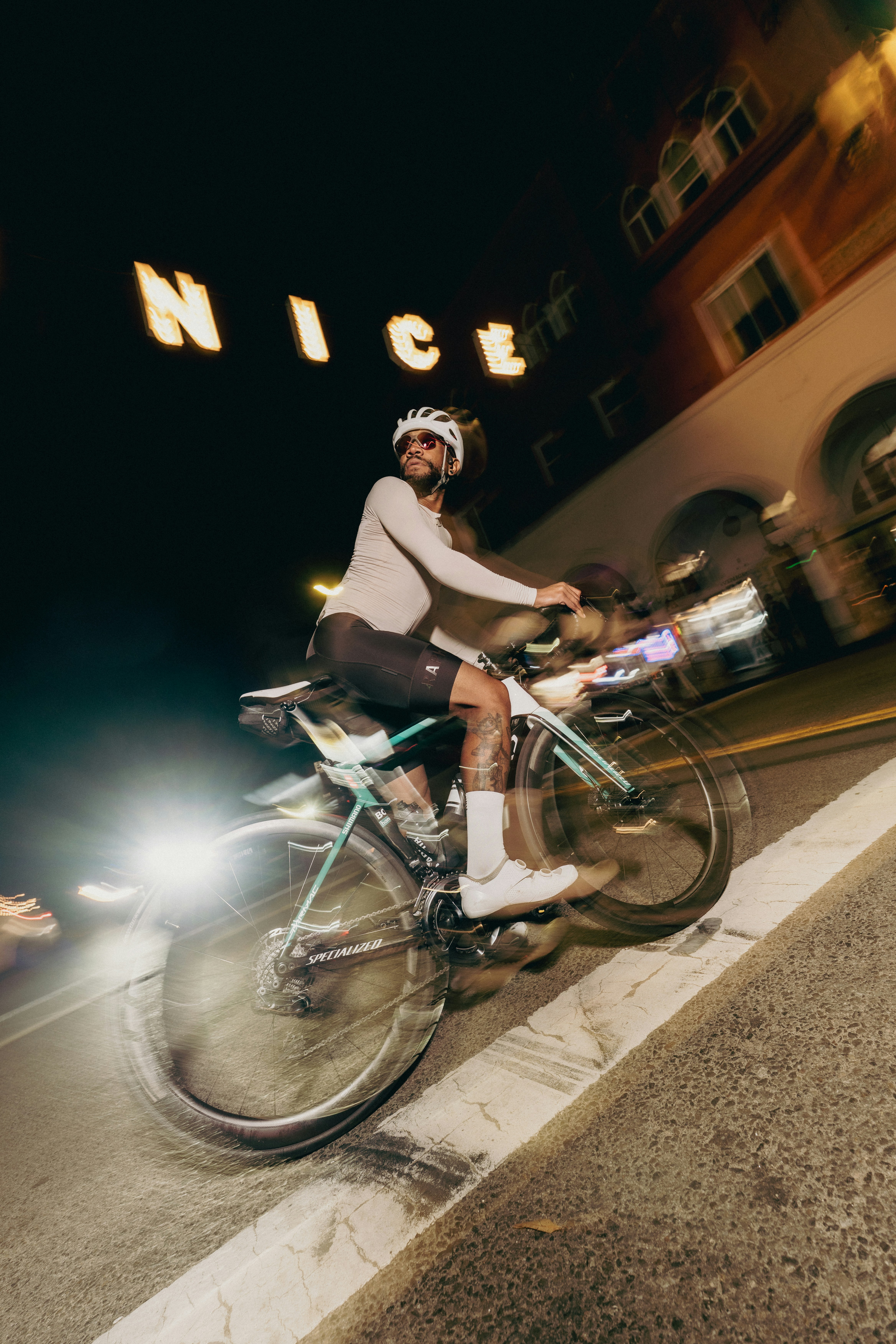 Cyclist rides by "nice" sign at night.
