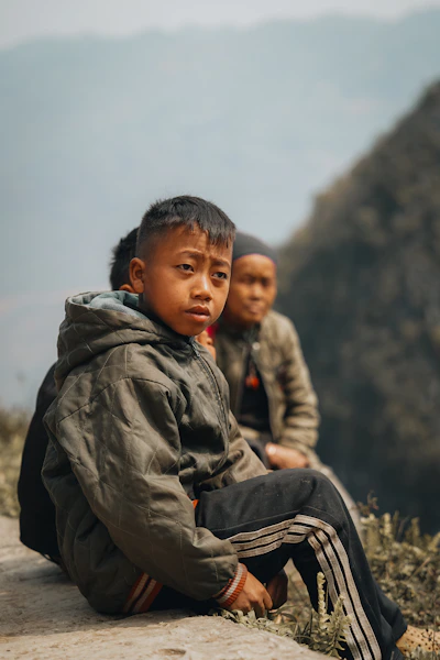 Three young boys sit outdoors, looking forward.