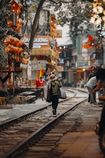 A person walks on train tracks in a vibrant street.