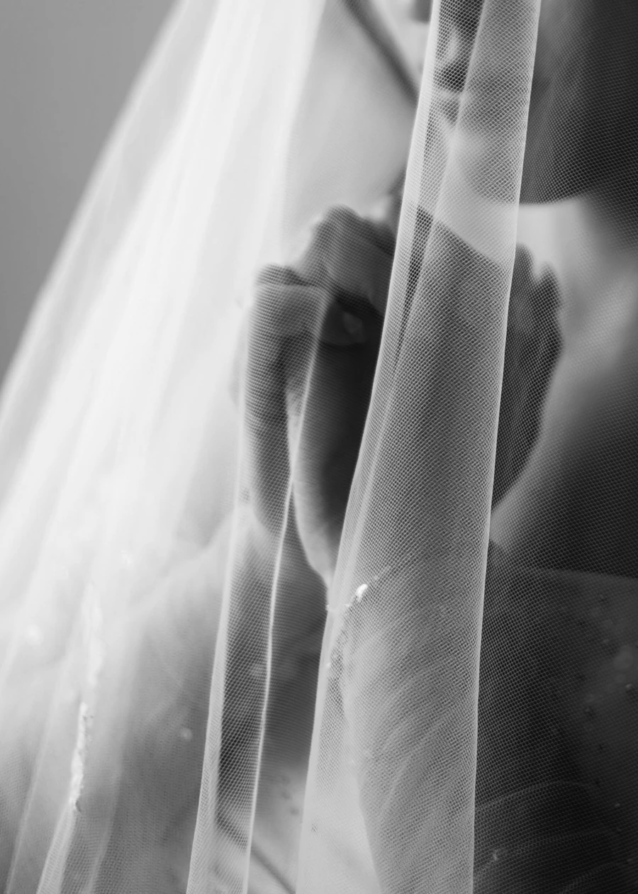A black-and-white editorial portrait of a bride veiled in soft light