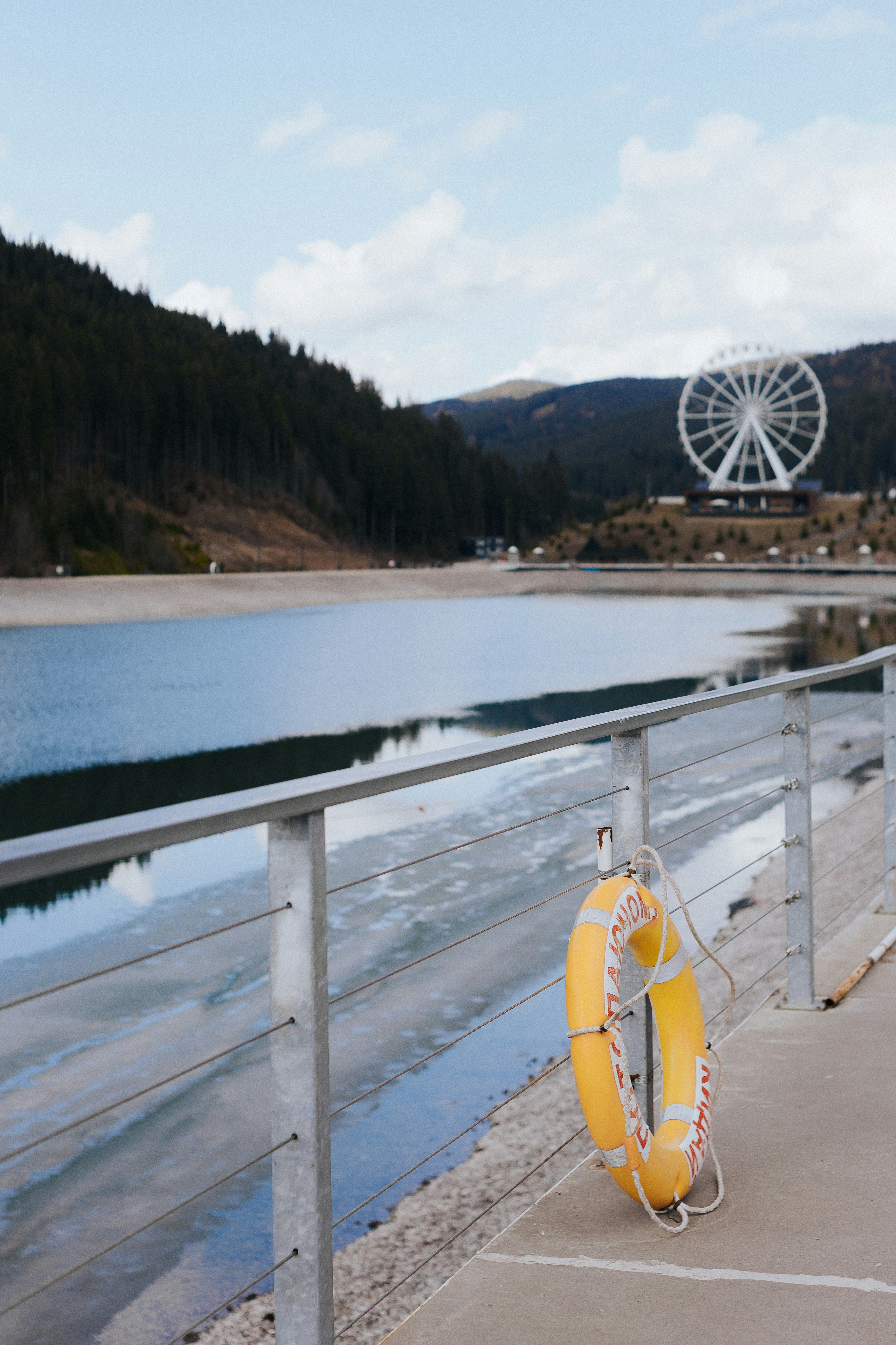 A life ring hangs by a lake with a ferris wheel.