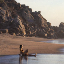 Woman sits on a beach at sunset.