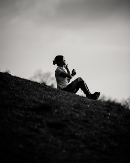 Woman sits on a hill, seemingly deep in thought.