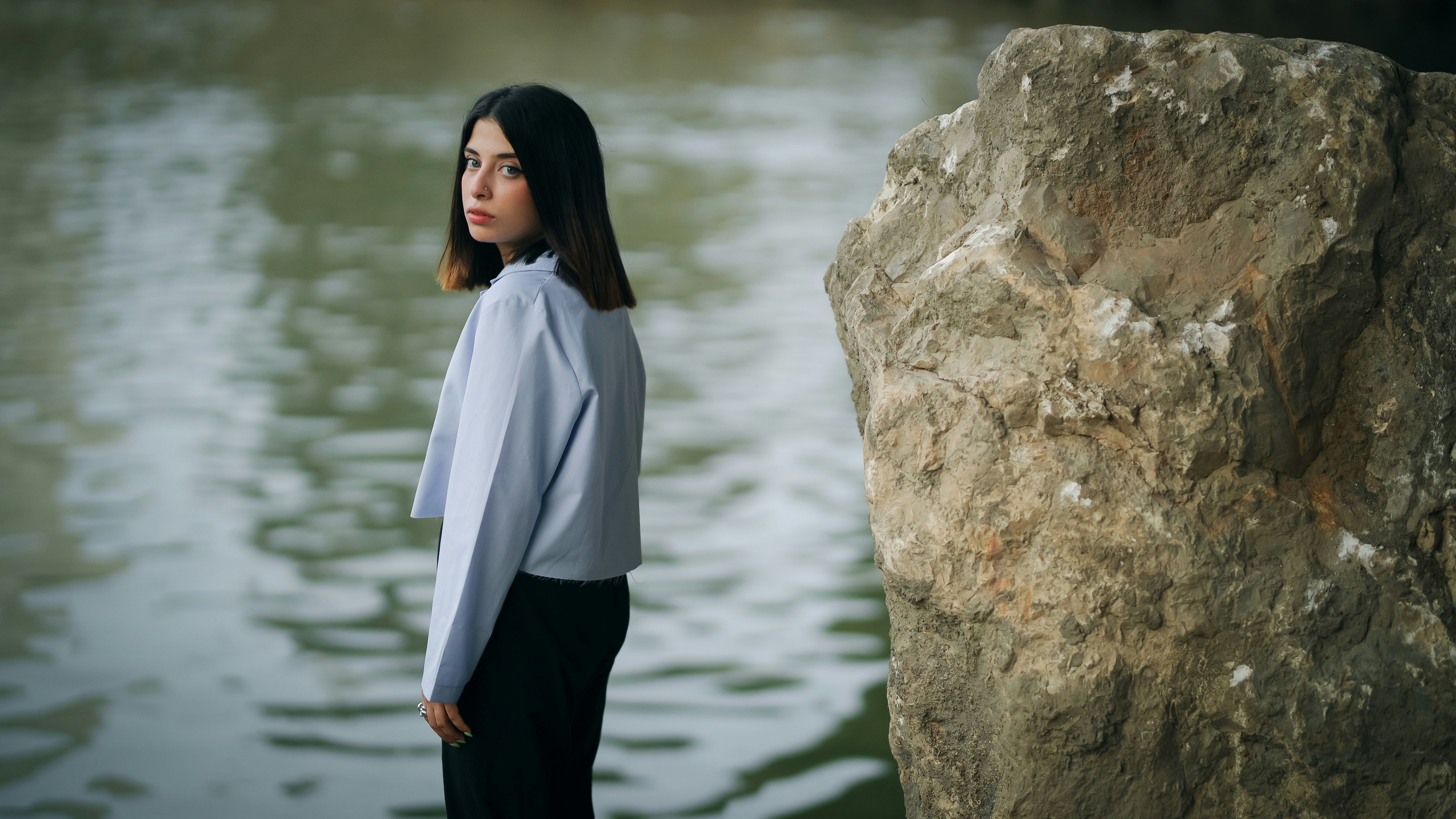 女性は湖のそばに立って肩越しに見ています。