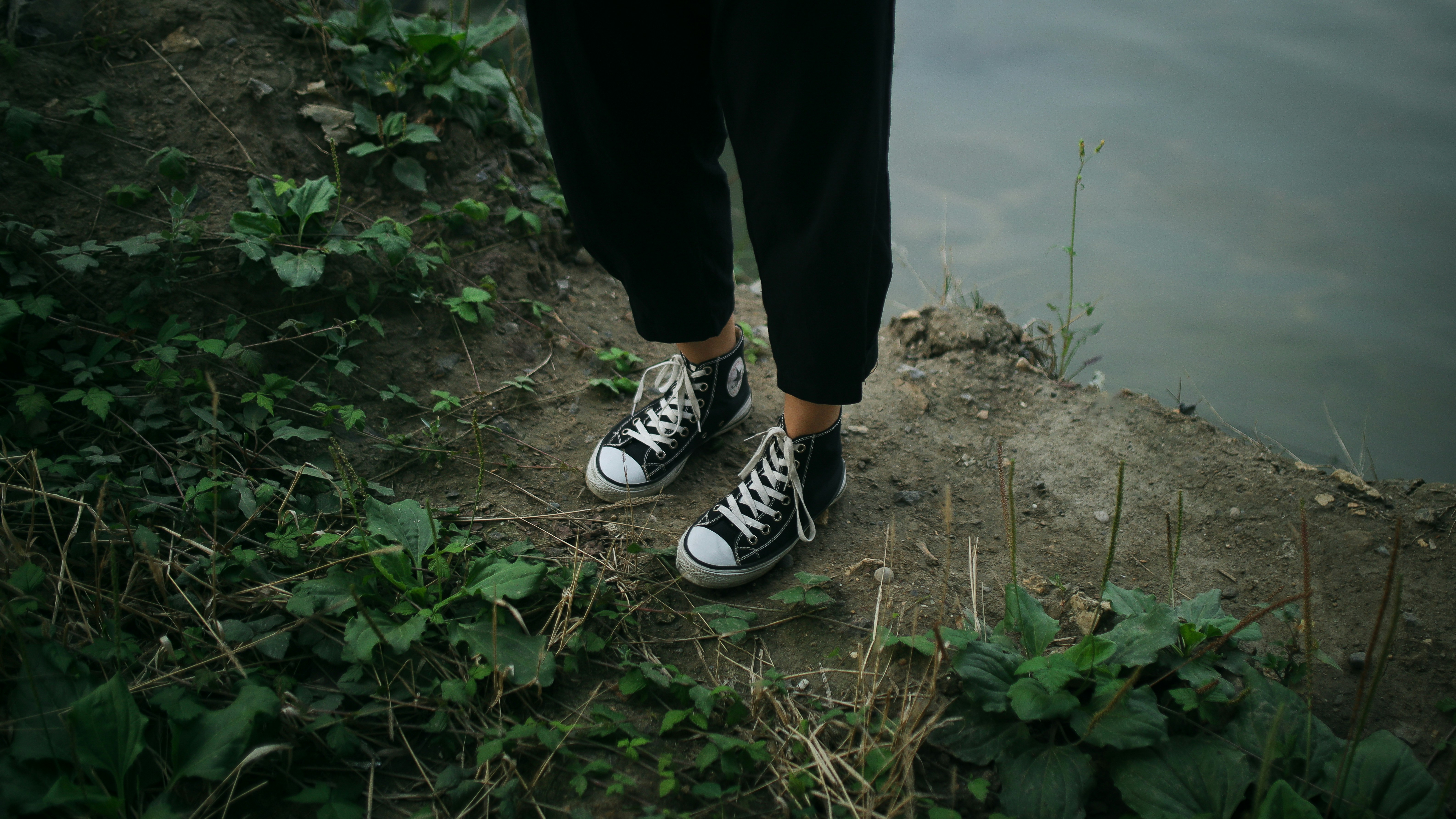 黒いズボンとスニーカーを履いて水辺に立っている人物。