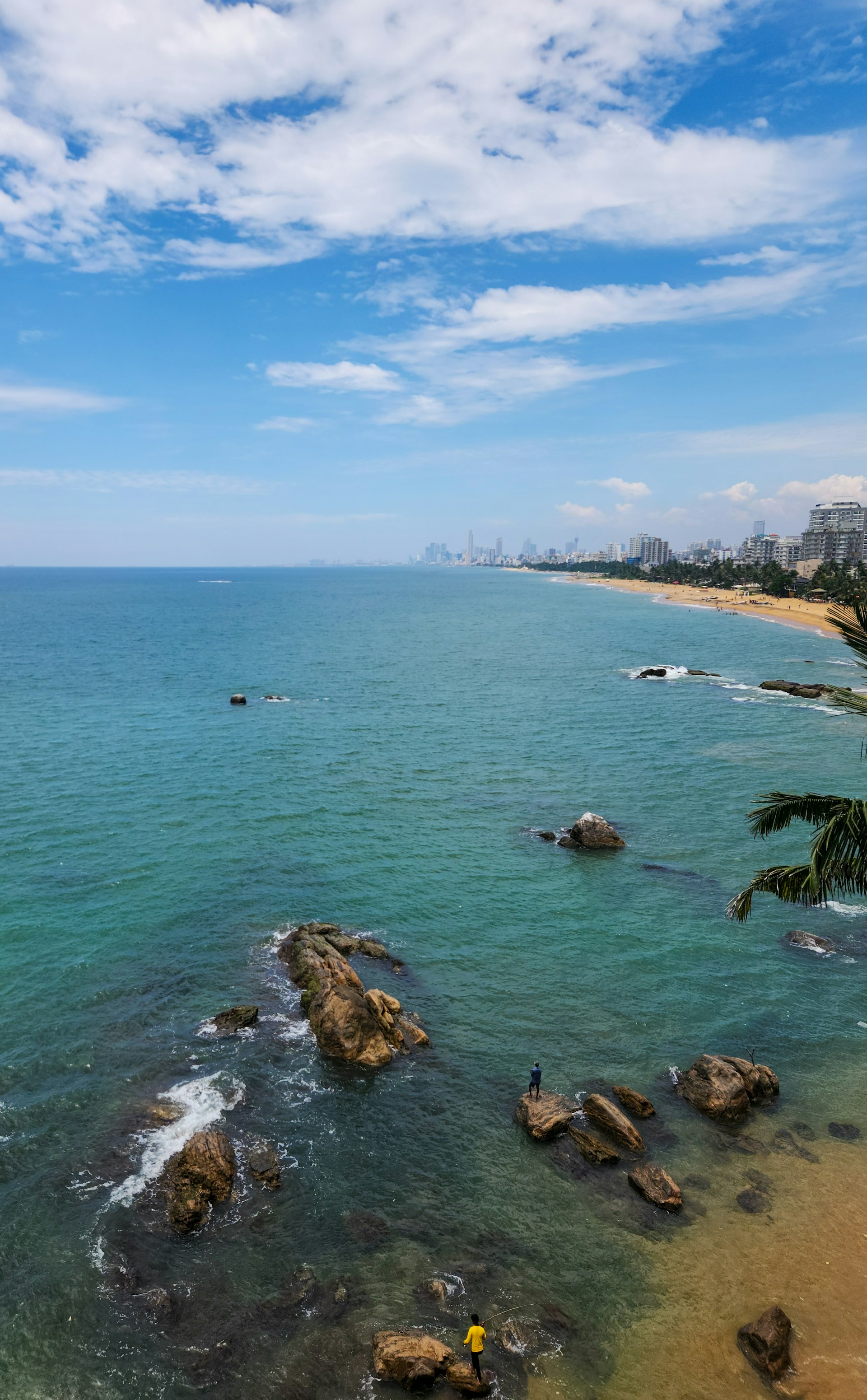 Coastal view with beach, sea, rocks, and buildings.