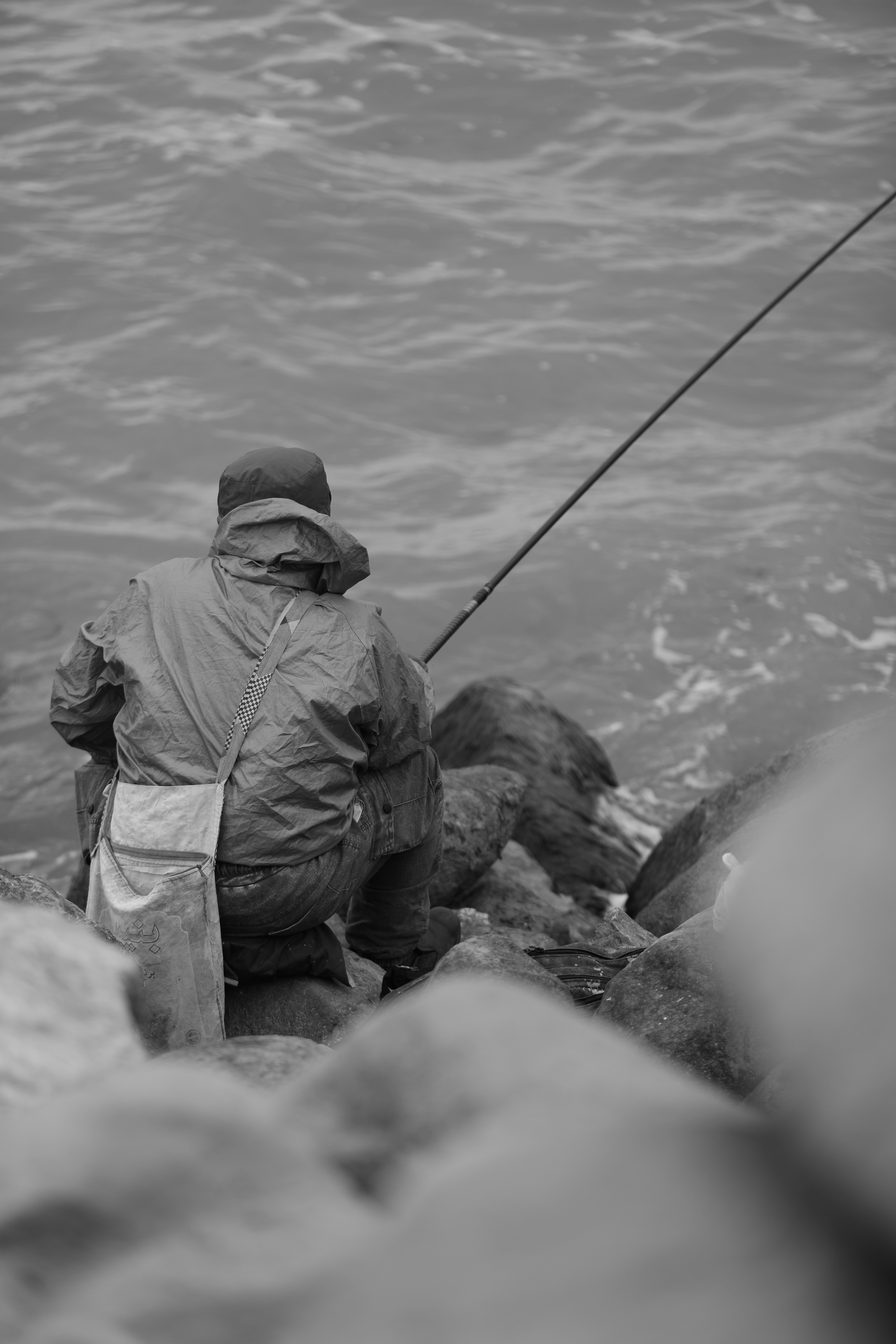 A fisherman fishes by the rocky seashore.