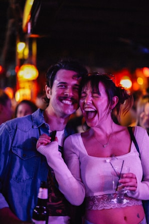 Couple smiles and laughs in a crowded bar.