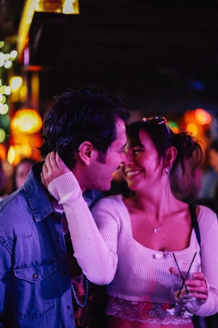 A couple smiles lovingly under colorful lights.