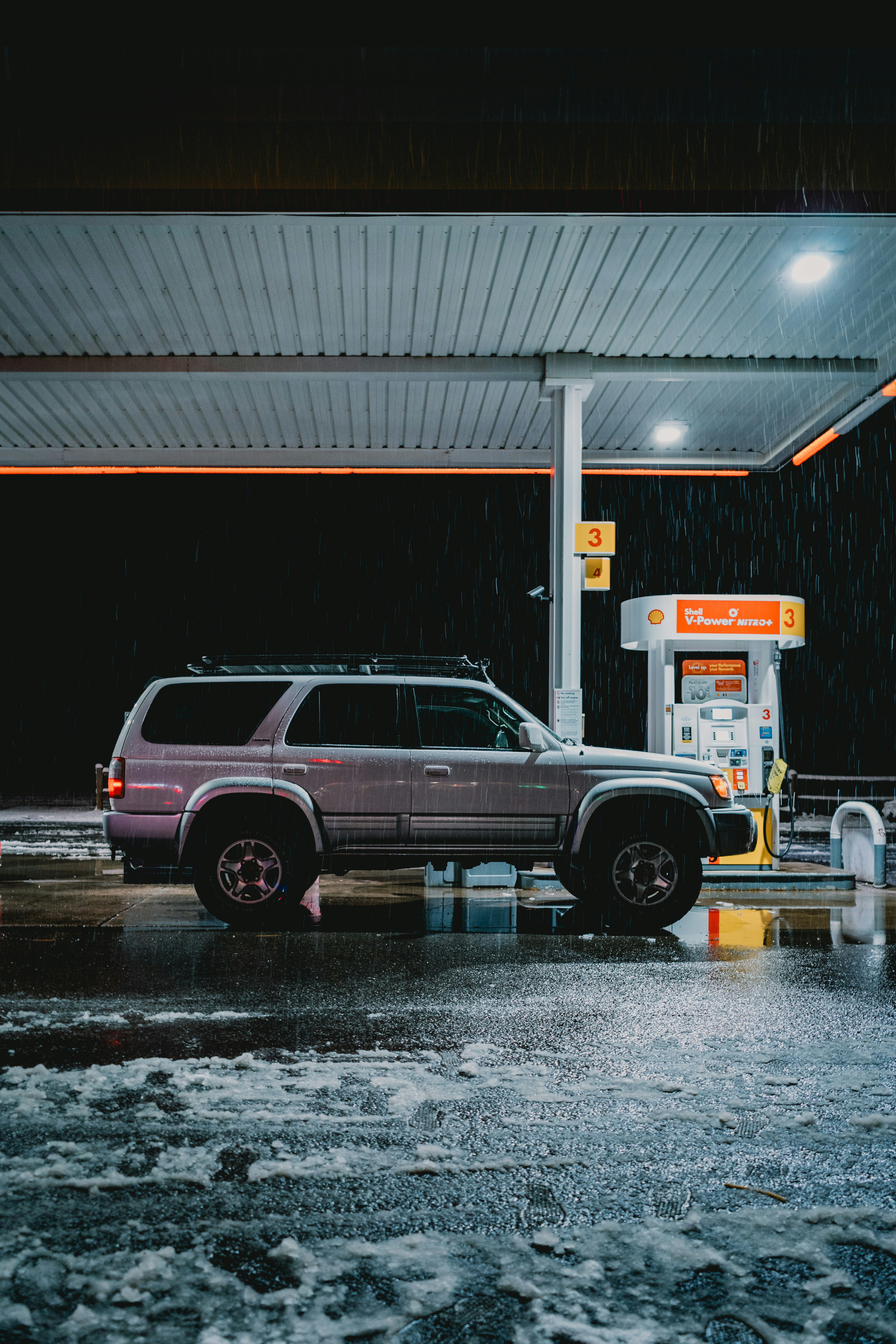 Ein silberner SUV steht im Regen an einer Tankstelle.