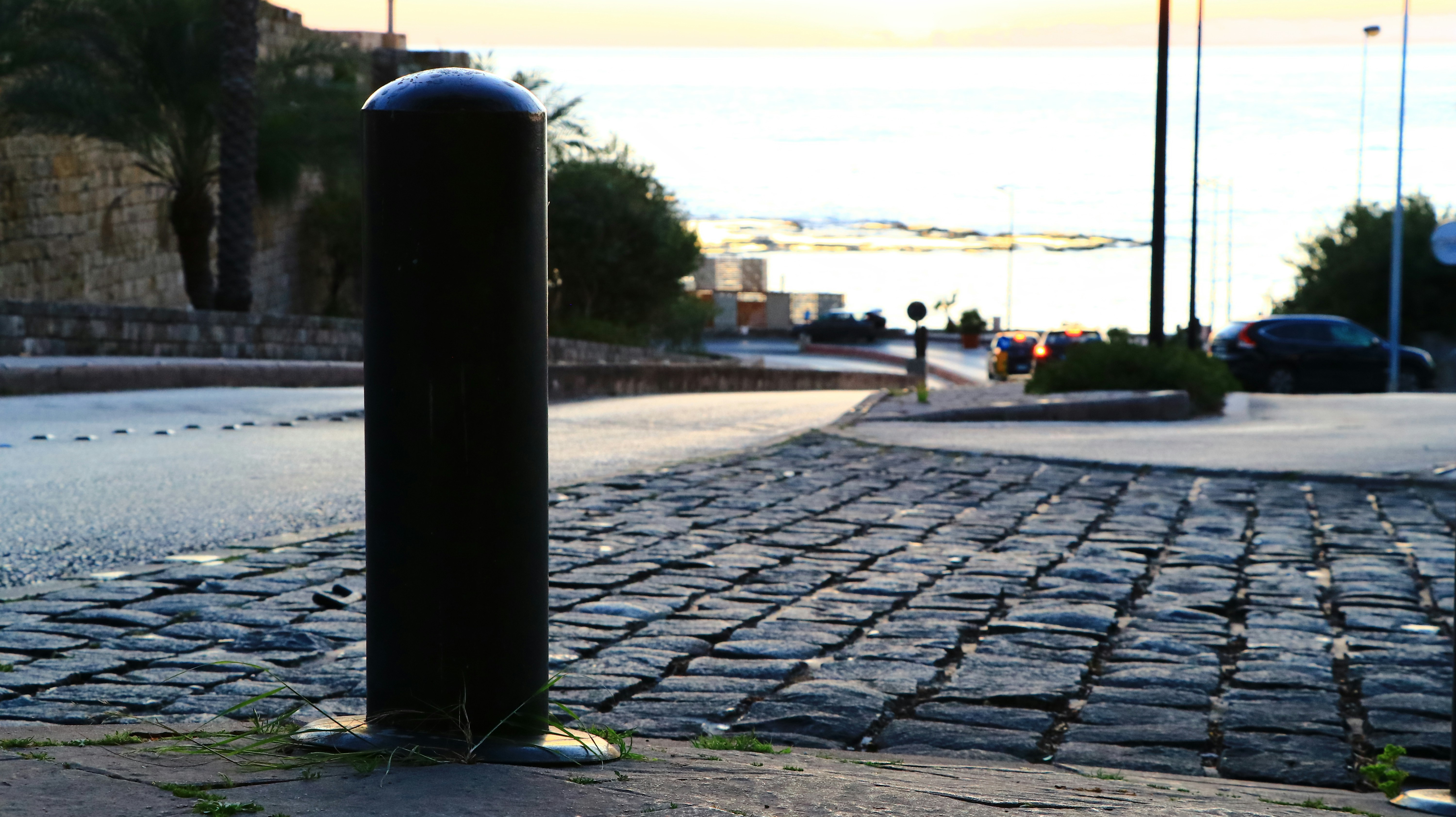 A bollard stands on a cobblestone street.