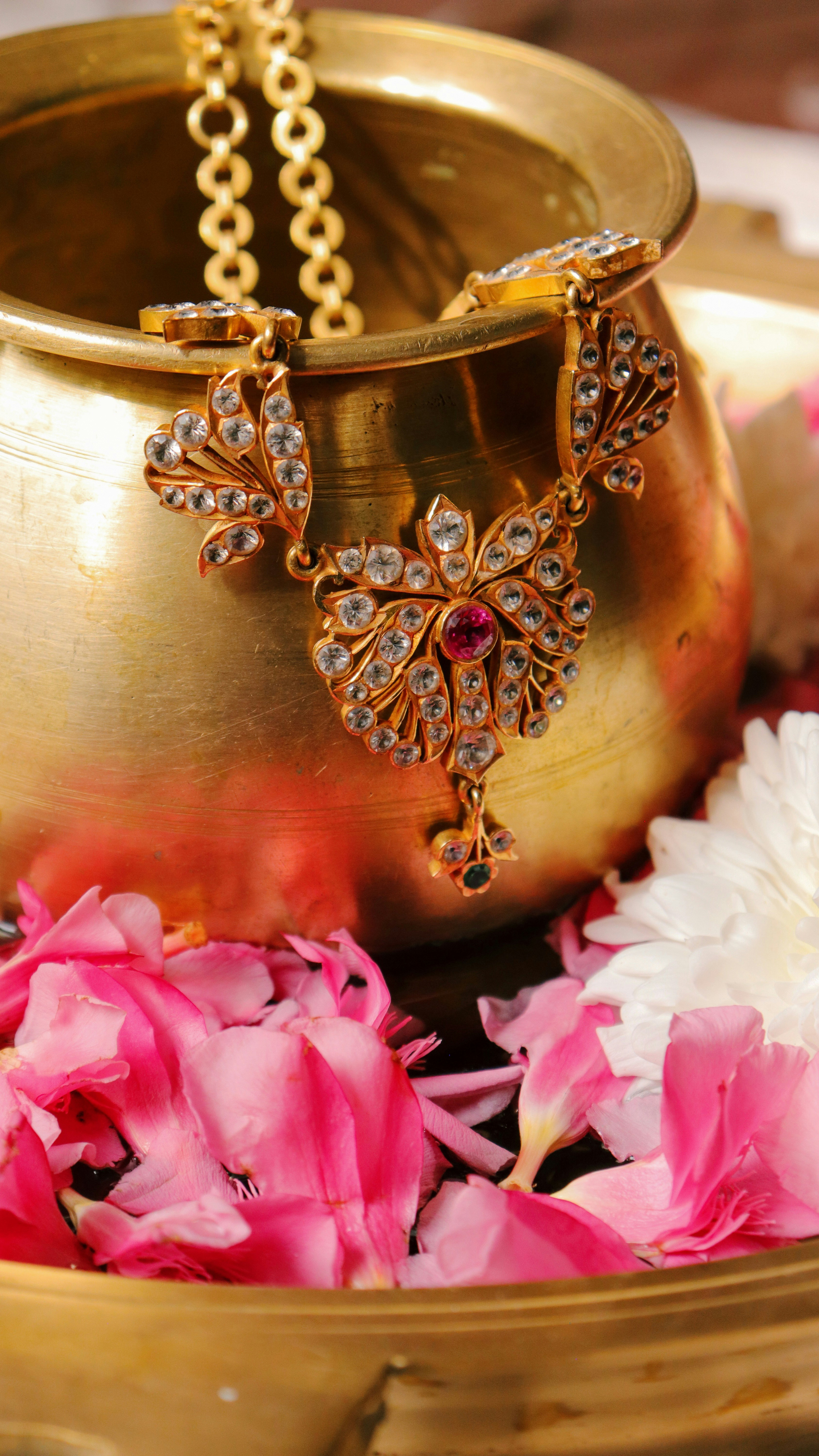 Golden necklace rests in a brass bowl with flower petals.