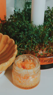 Jar of scrub sits near greenery.