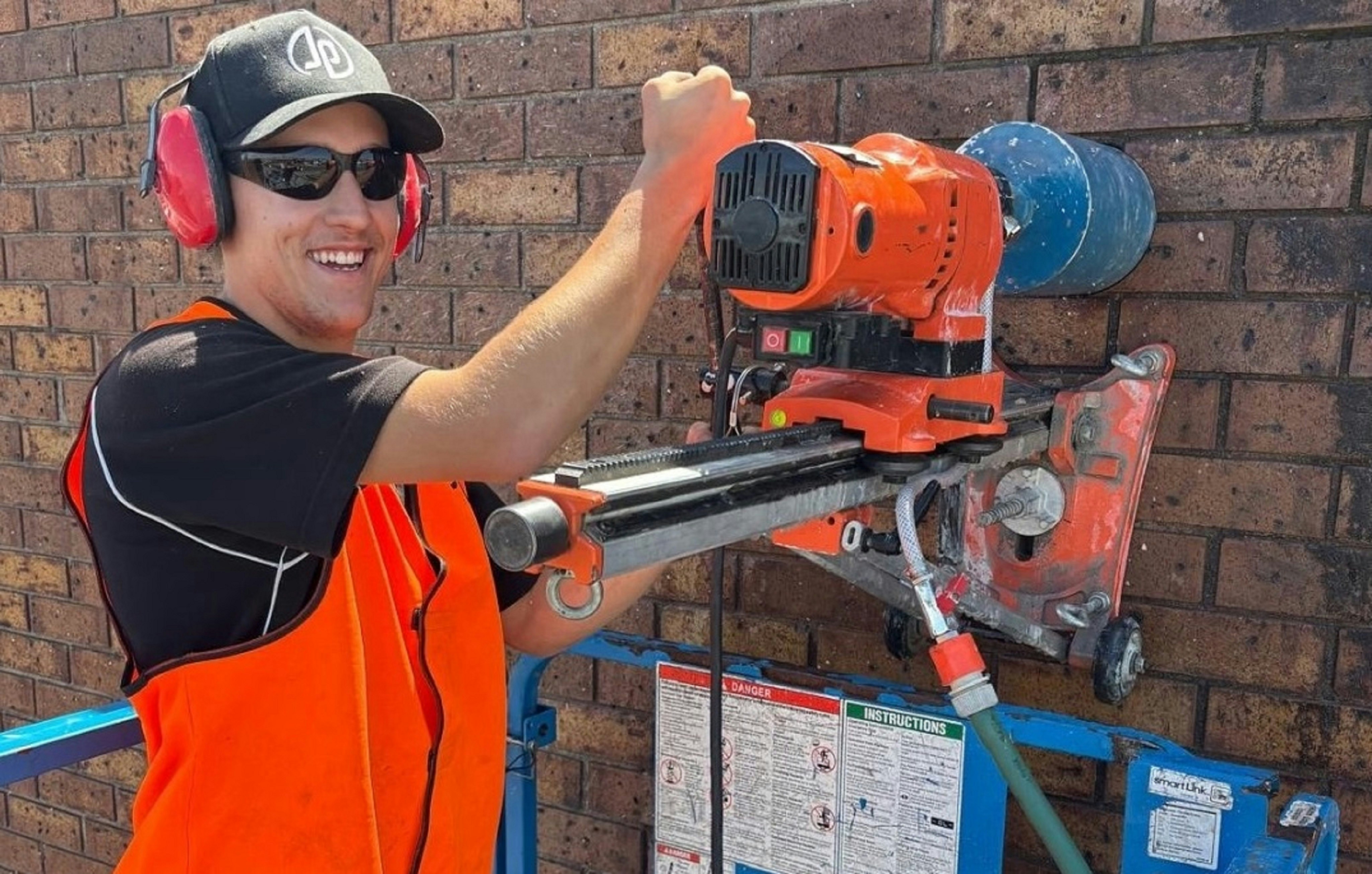 A worker is drilling a hole into a brick wall.