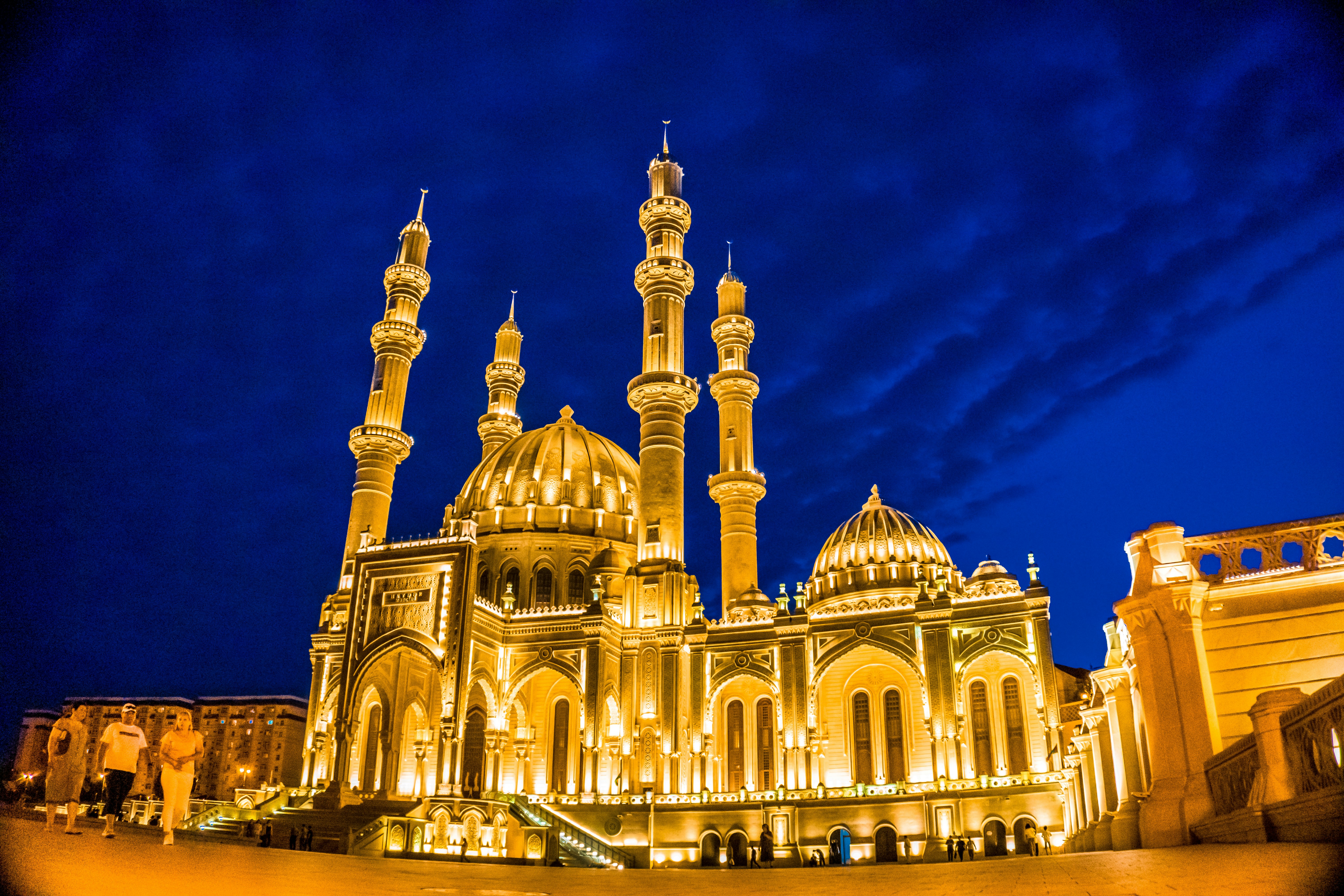 Illuminated mosque stands tall against a dark blue sky.