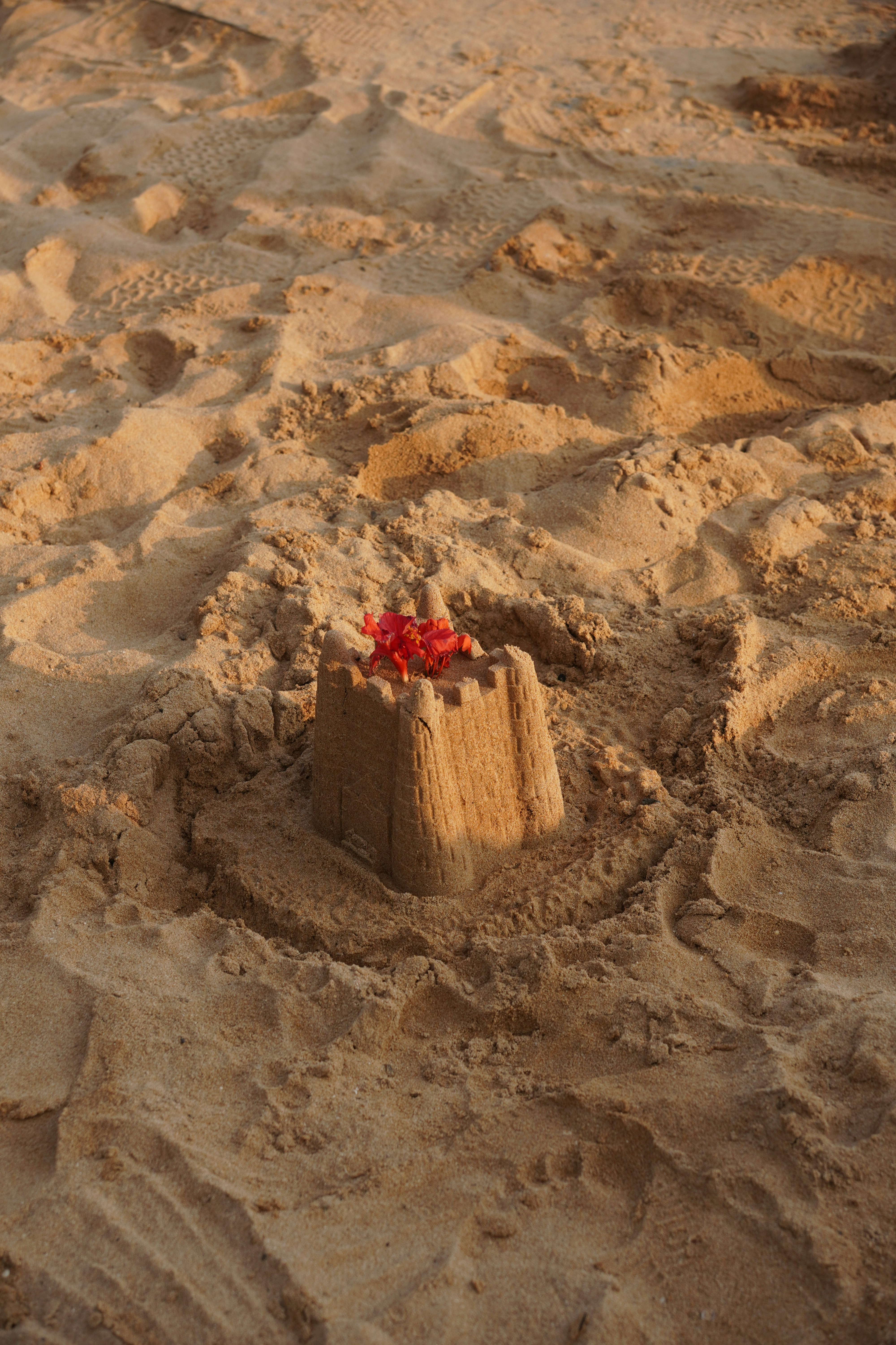 Un castillo de arena decorado con flores rojas.
