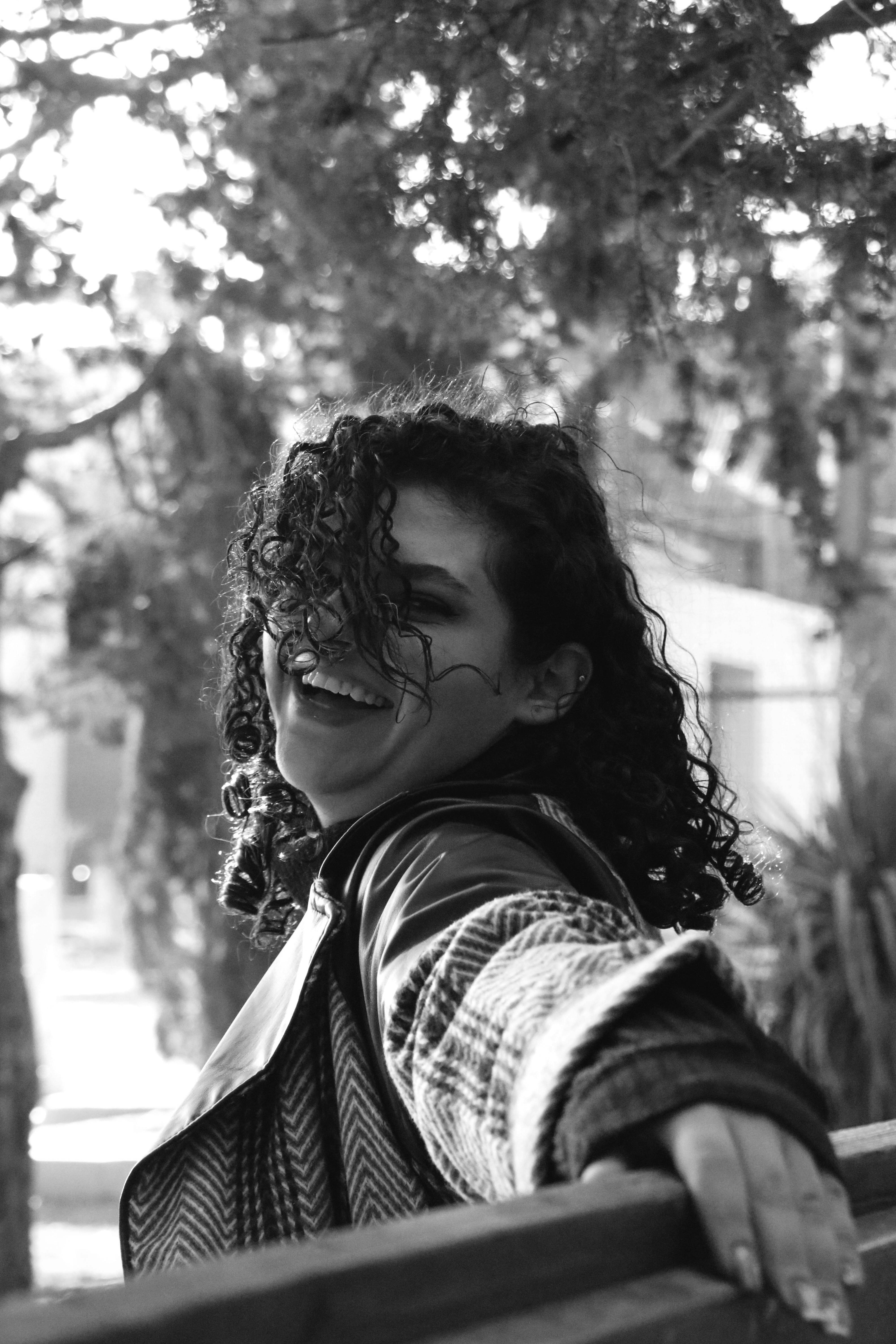A woman with curly hair laughs outdoors.