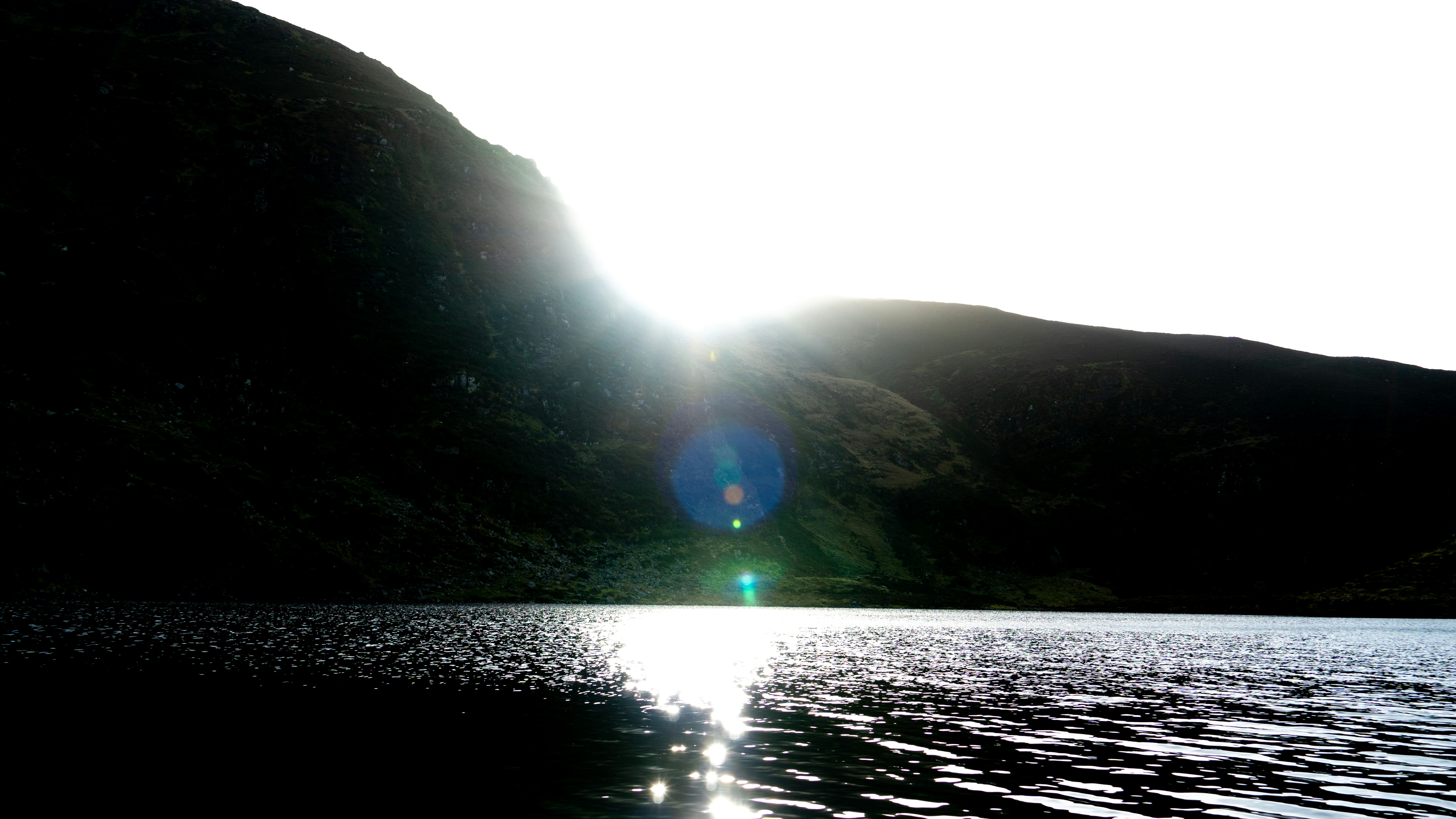 Sun shining over a lake with mountainous backdrop.