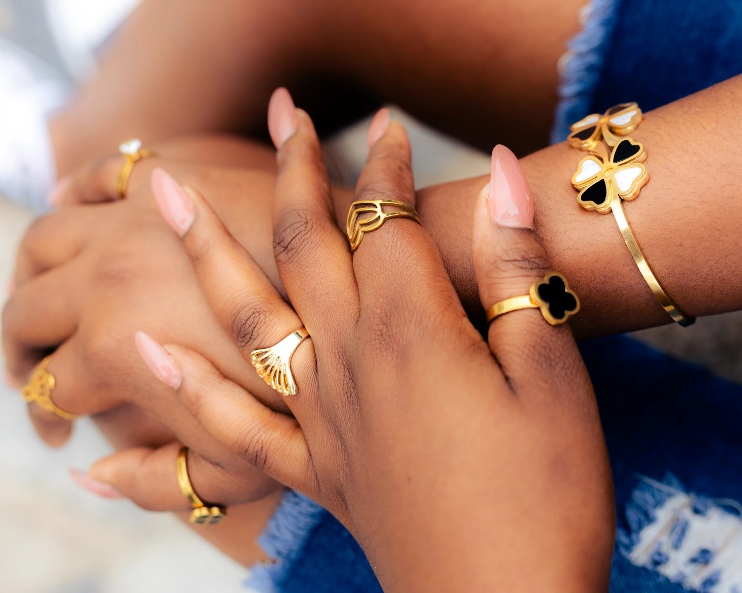 Two hands of different skin tones resting together, wearing five slim gold rings between them