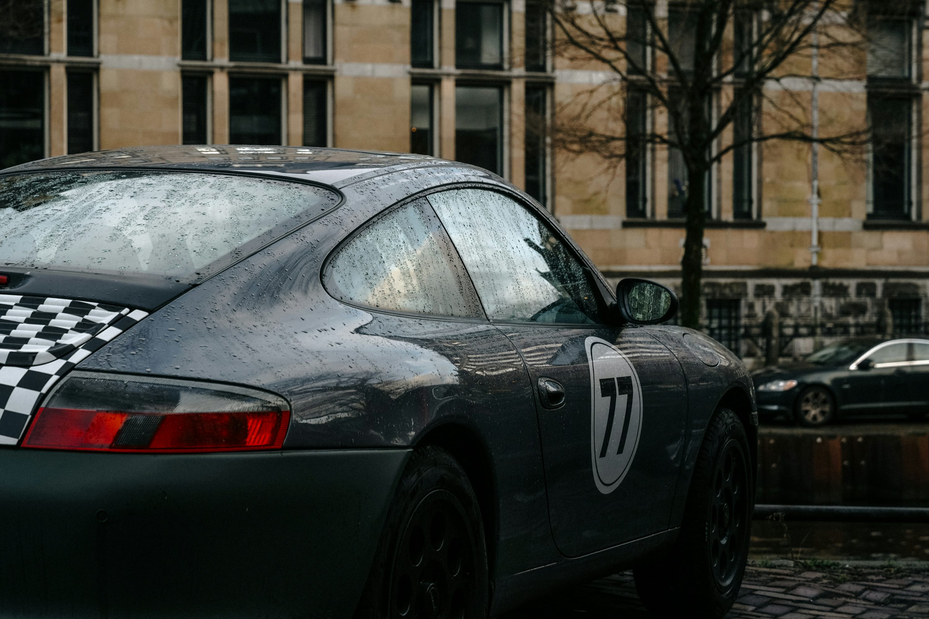 A gray porsche with racing stripes is parked.